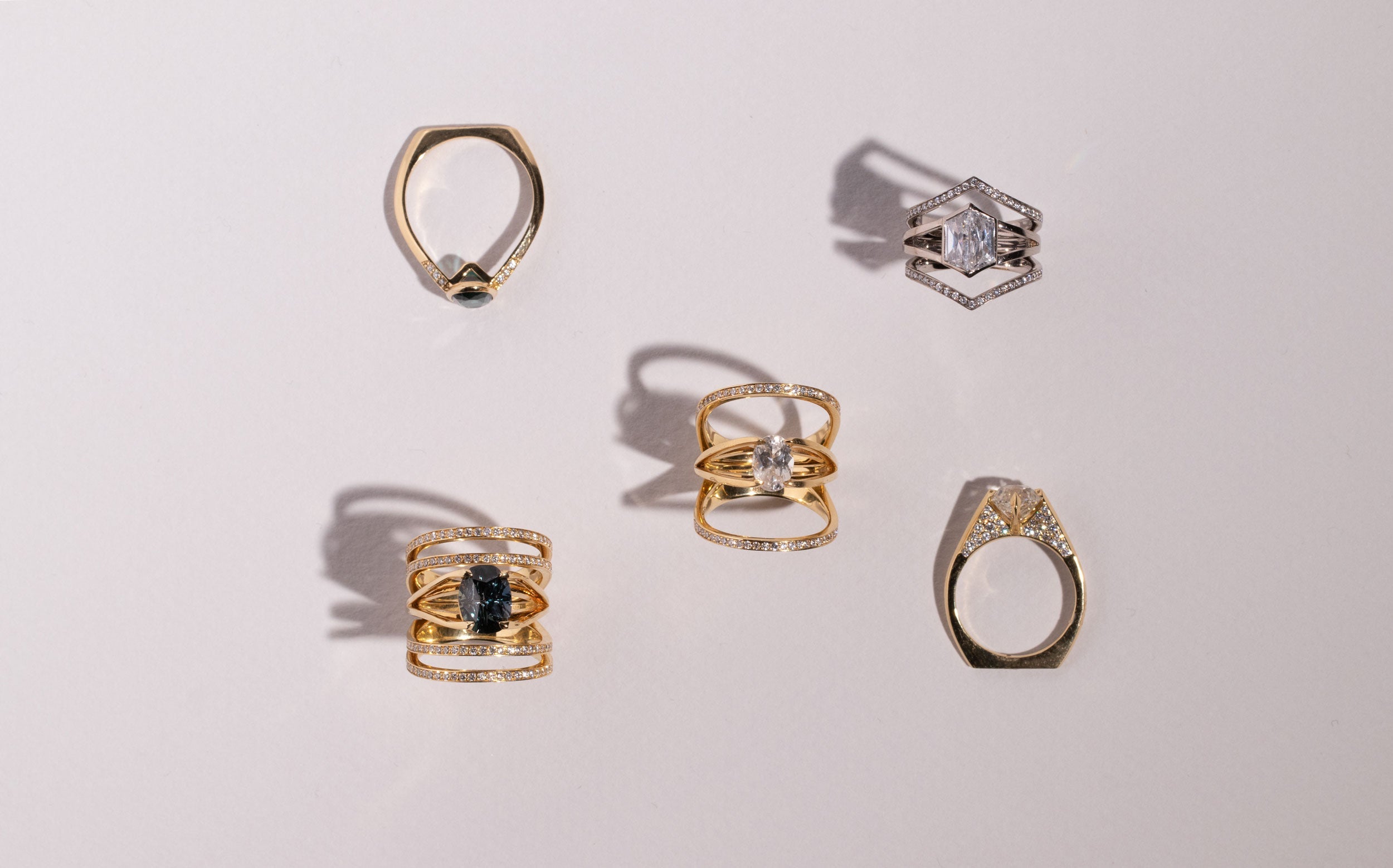 A stylish display of hands adorned with various gemstone rings, showcasing a blend of modern and elegant designs. The rings feature intricate patterns and materials, set against a dark background for a dramatic effect.