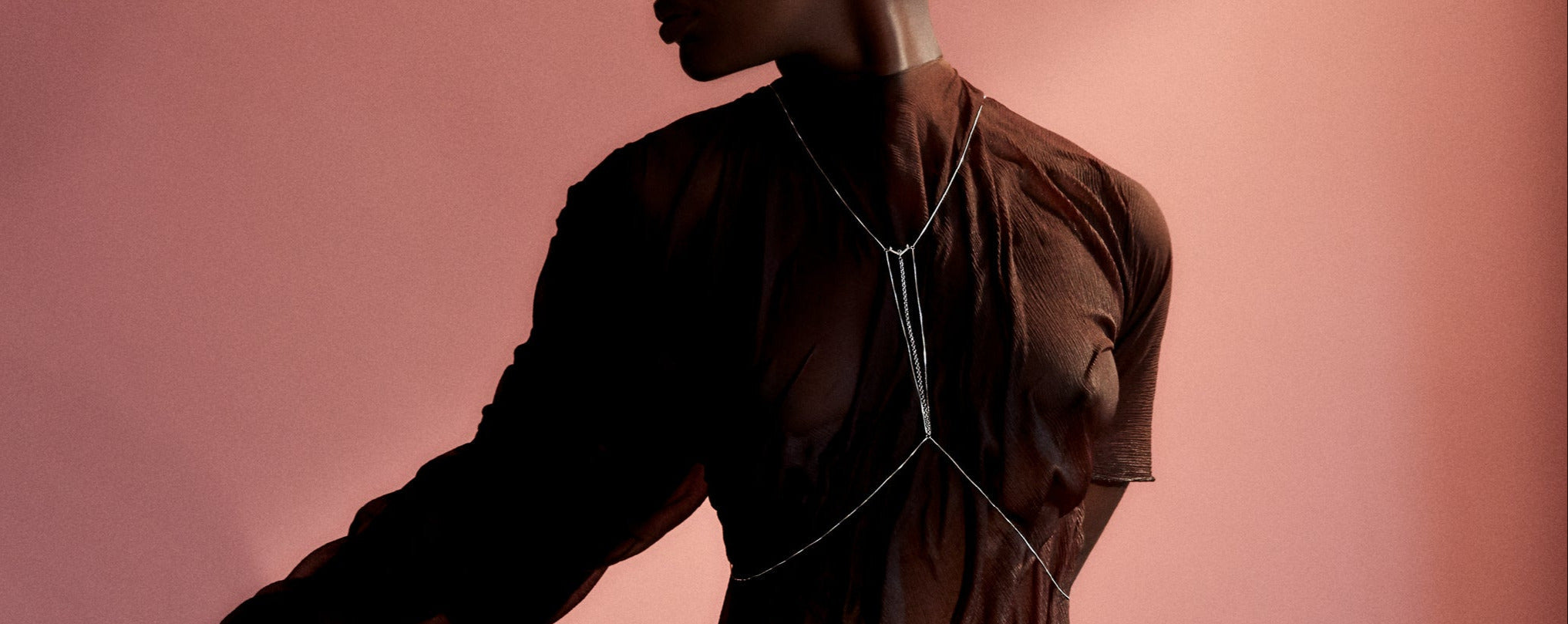 A model wearing a minimalistic body chain over a light grey top, showcasing the elegant design against a simple backdrop. The bodychain adds a stylish touch to her outfit, emphasizing the intricate details of the jewelry.