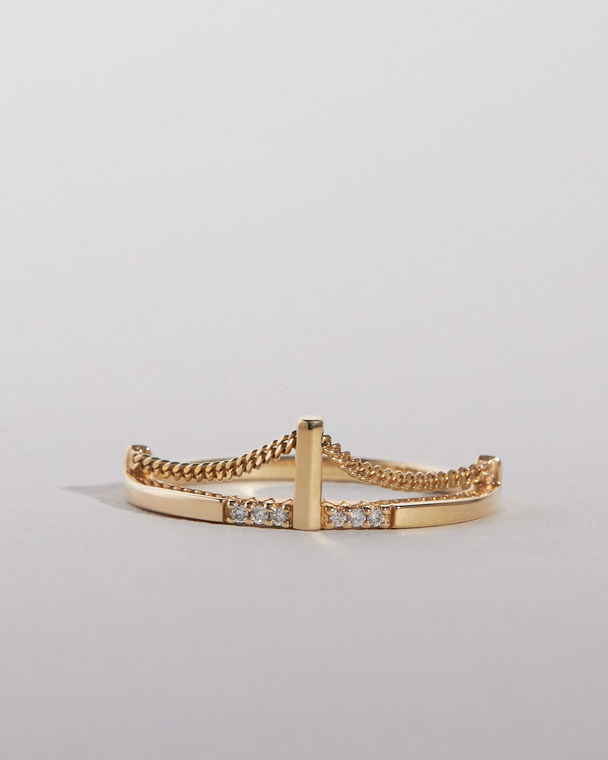 Gold ring inspired by the Brooklyn Bridge with gold chain and diamond accents on a light gray background