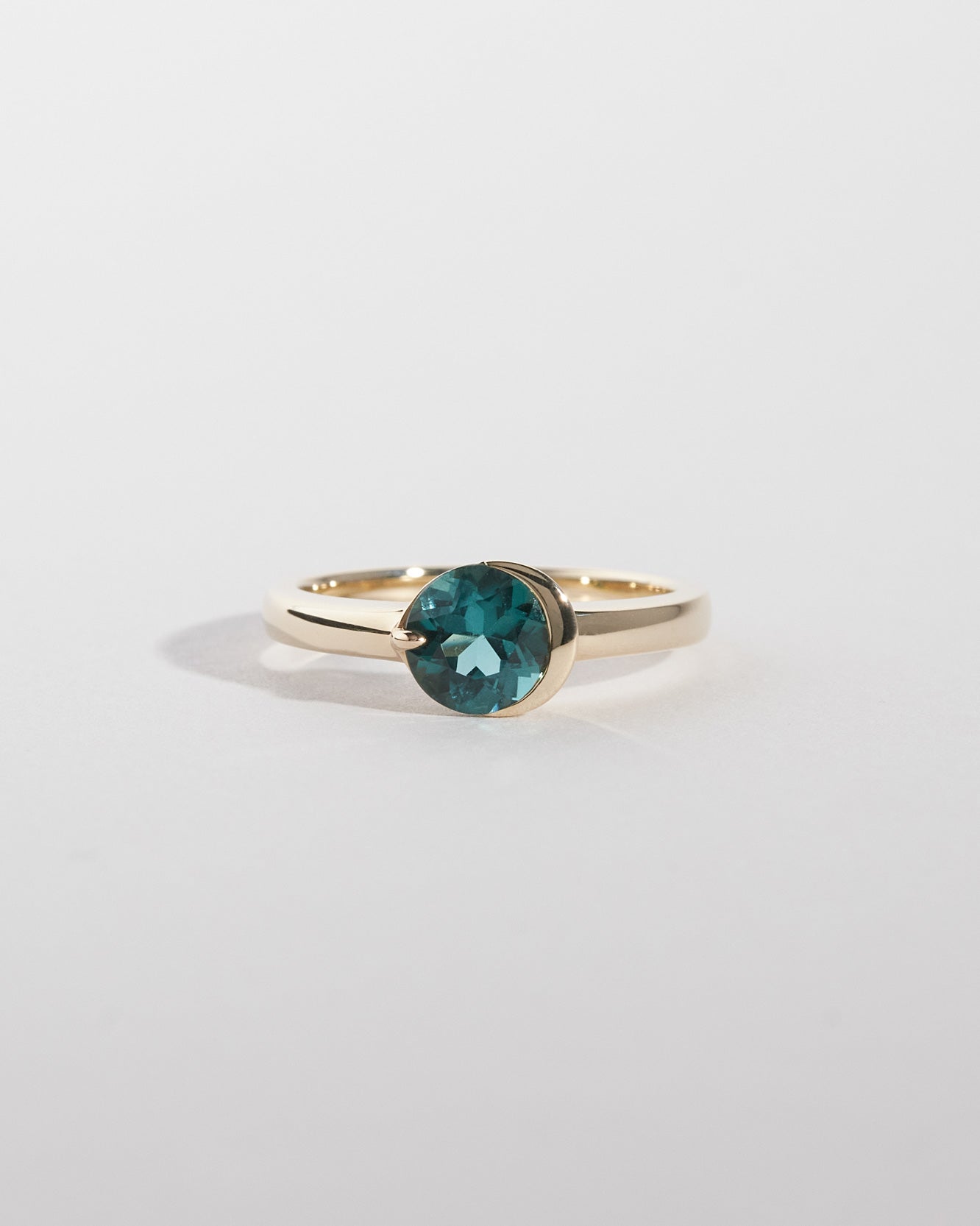 Gold ring with a green gemstone on a light gray background