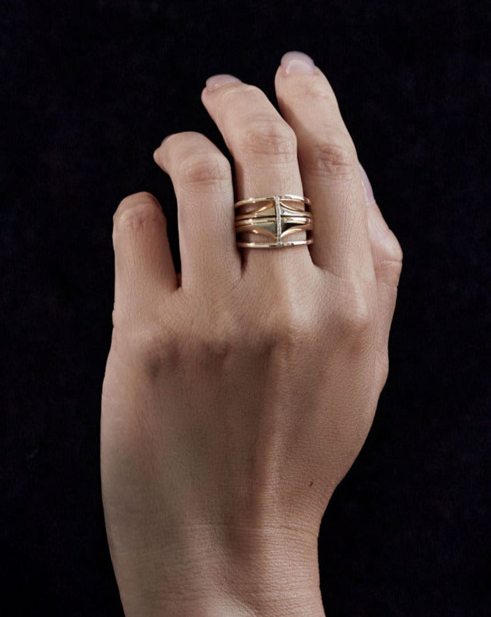 A hand adorned with the Kaleidoscope Mini Split Ring set, beautifully layered to highlight the refinement of the 18k Fairmined gold design against a dark background.