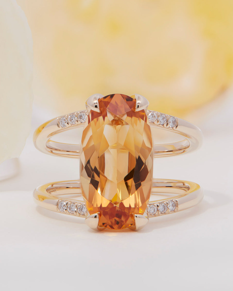 Illuminate Engagement Ring Signature Collection presenting a luxurious oval orange gemstone with diamond embellishments, exuding elegance against a gentle pastel setting.