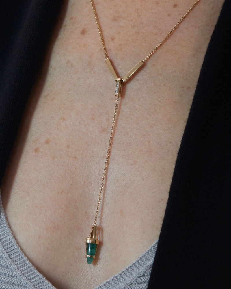 The Emerald Vantage Curio pendant elegantly displayed on a model, highlighting its unique design and the captivating Brazilian Emerald Cabochon, a symbol of luxury and connection to nature.