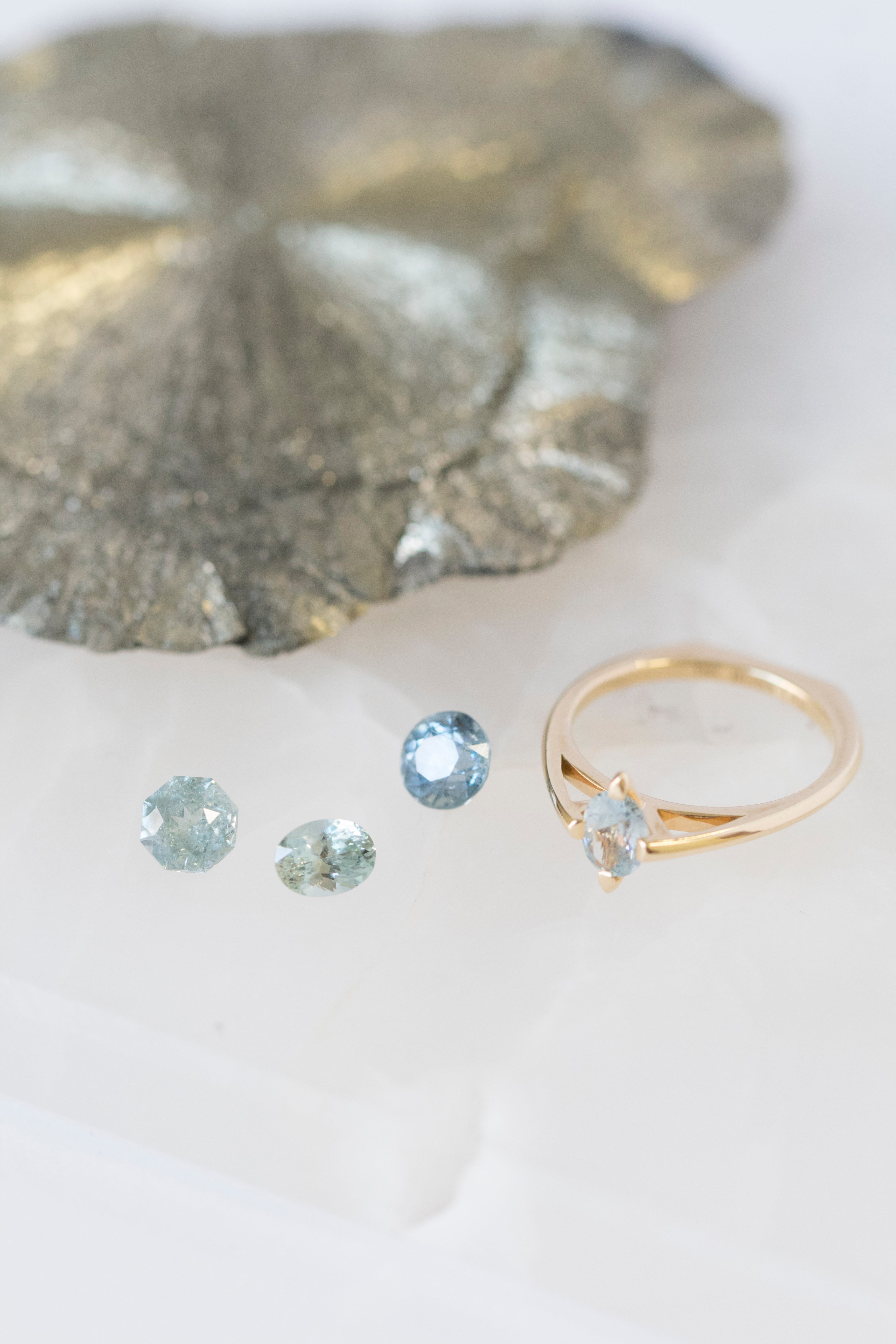 A collection of Montana sapphires beside a minimalist gold ring, illustrating the essence of Bliss Lau's minimalist arc, minimalist rise, and minimalist pave.