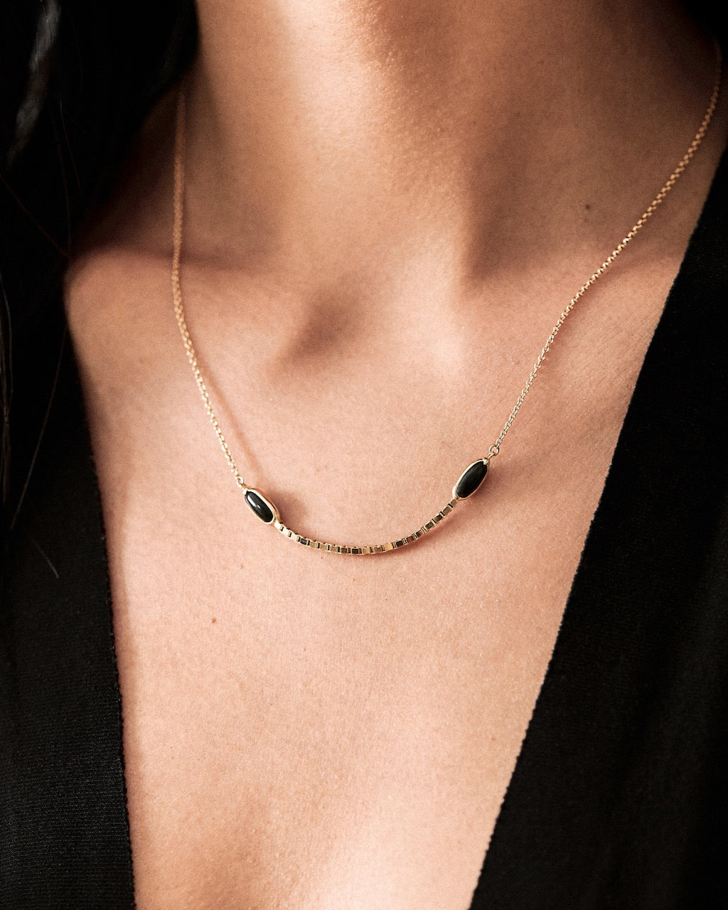 gold Necklace with black jade worn by a person against a dark background