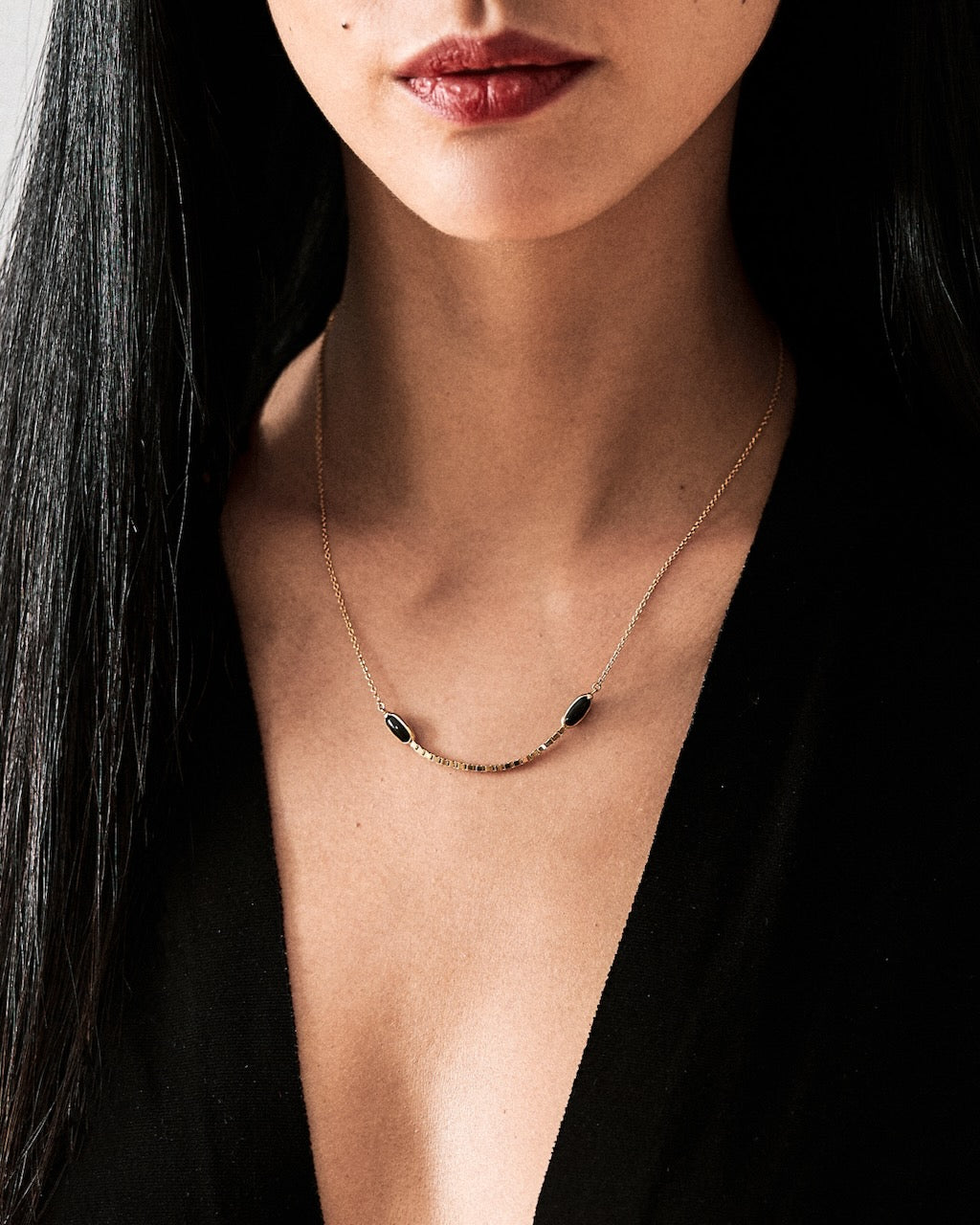 gold Necklace with black jade worn by a person with long dark hair and red lipstick.