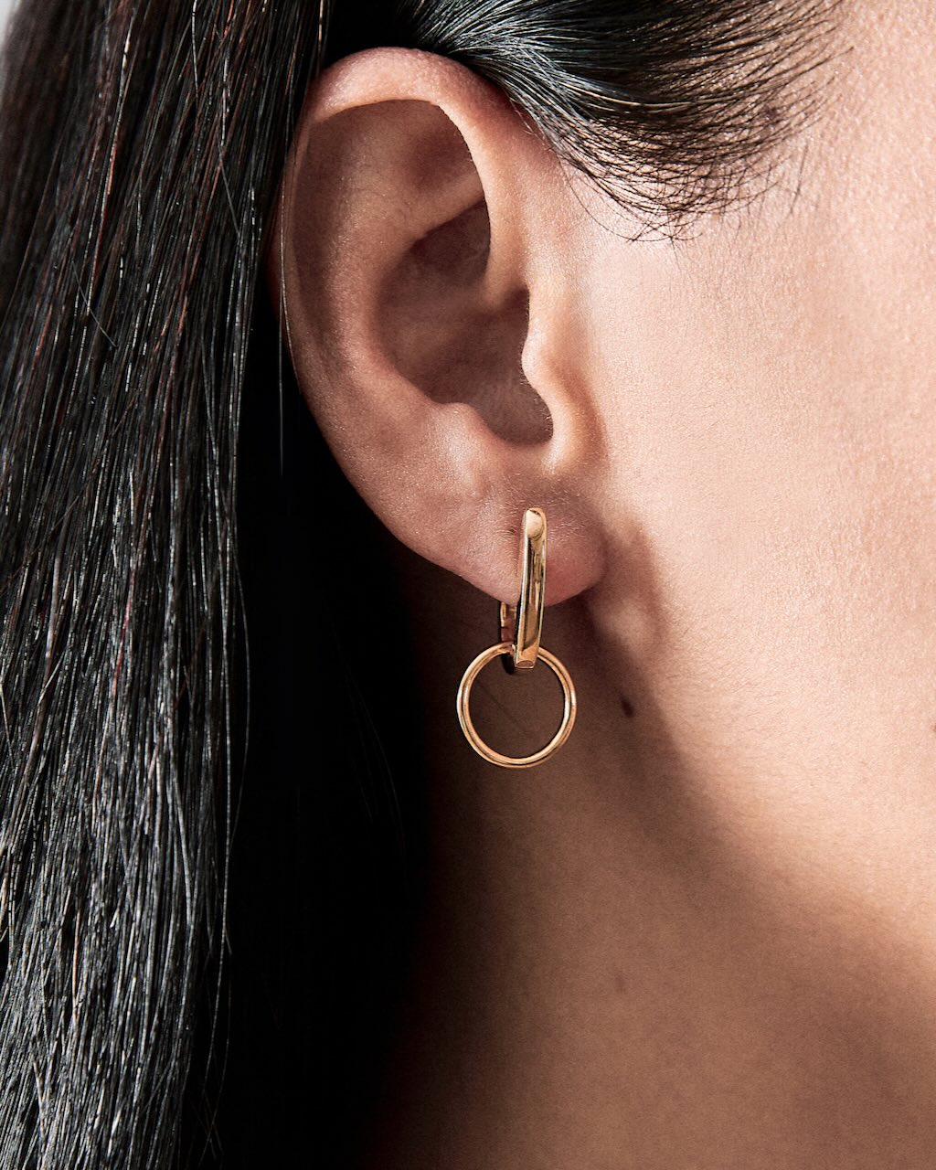 Close-up of an ear wearing a gold hoop earring with dark hair.