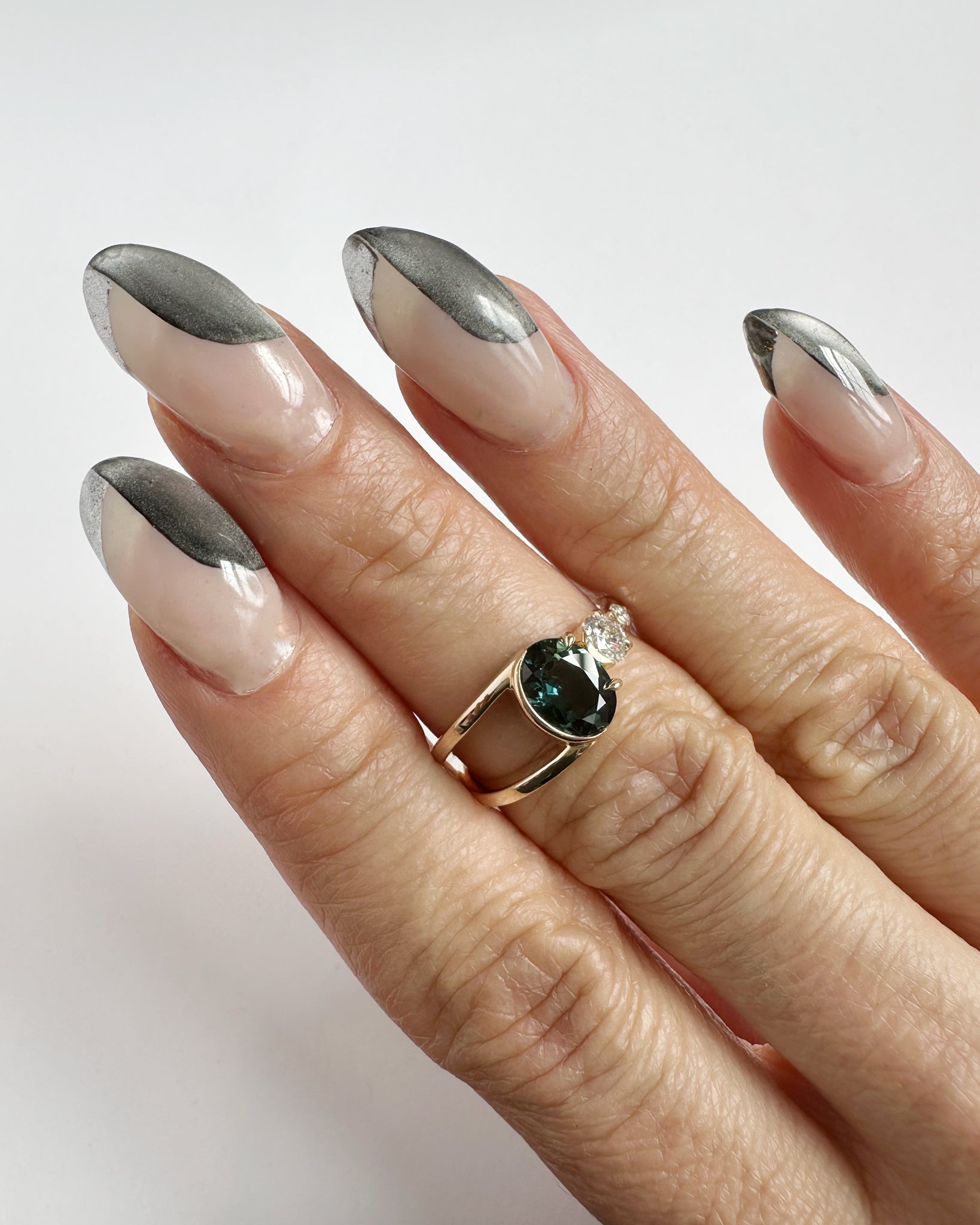 Bright Ring Green Sapphire worn on a hand with stylish nails, displaying the elegant design featuring a blend of a deep blue-green sapphire and diamond in 14K gold.