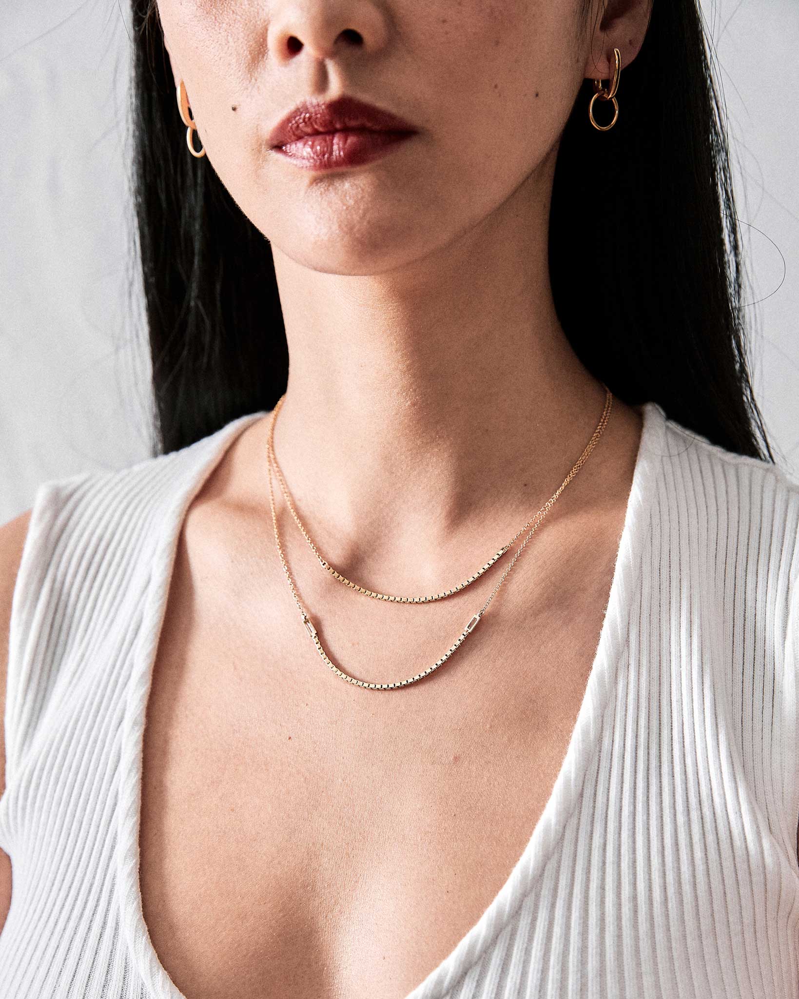 Stylish model wearing Nuance Hoop Huggie Earring in 18k Gold alongside a layered gold necklace, highlighting luxury and sophisticated jewelry pairing.