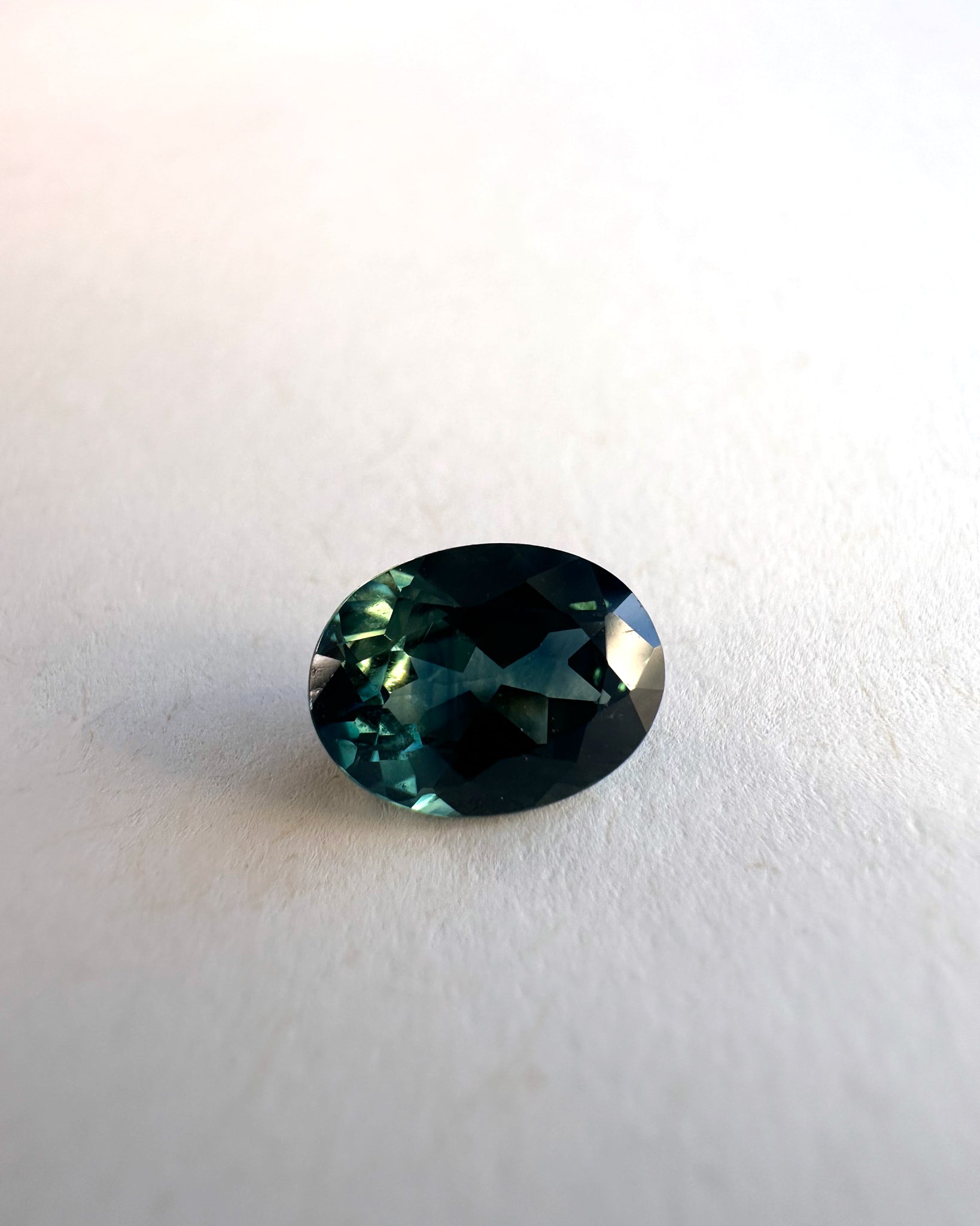 High-quality image of a deep blue-green oval parti Australian sapphire, showcasing its brilliance and color, highlighting the unique gemstone featured in the Bright Ring Green Sapphire design.