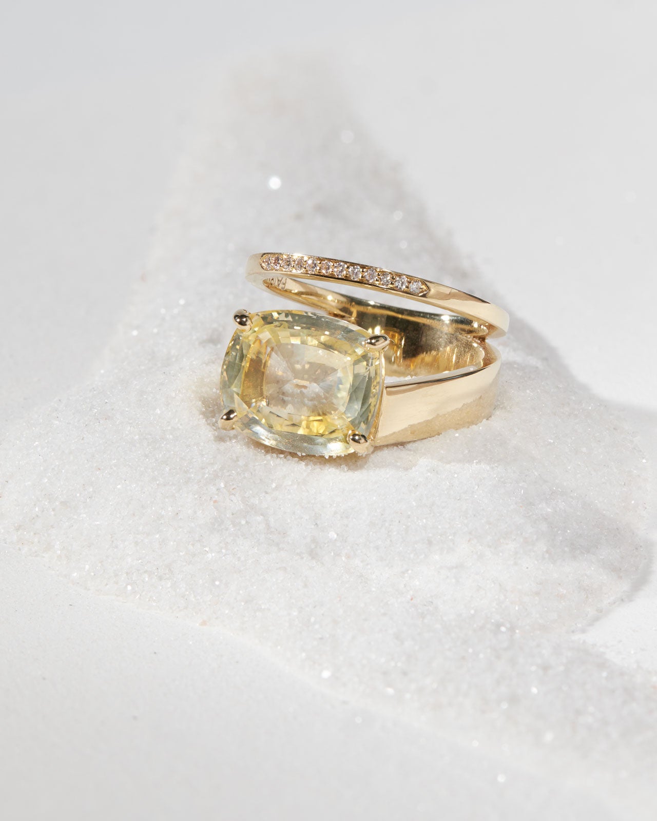 Elegant Wanderer IV Ring with Yellow Sapphire, featuring a stunning cushion cut pale yellow sapphire set in Fairmined 18K Gold, adorned with natural white diamond pavé, beautifully displayed on a shimmering surface.