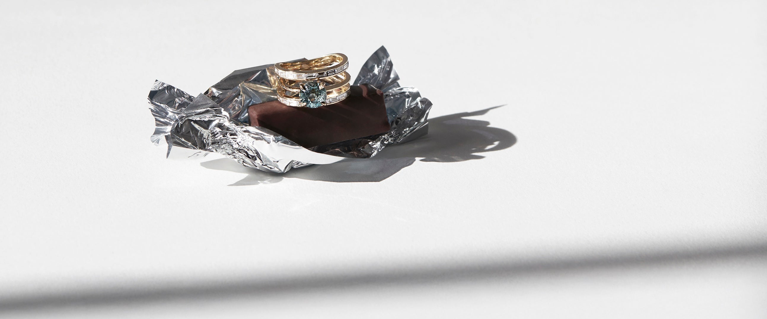Gold ring set with sapphire and diamond baguettes sitting on a piece of chocolate with wrapper on a white background
