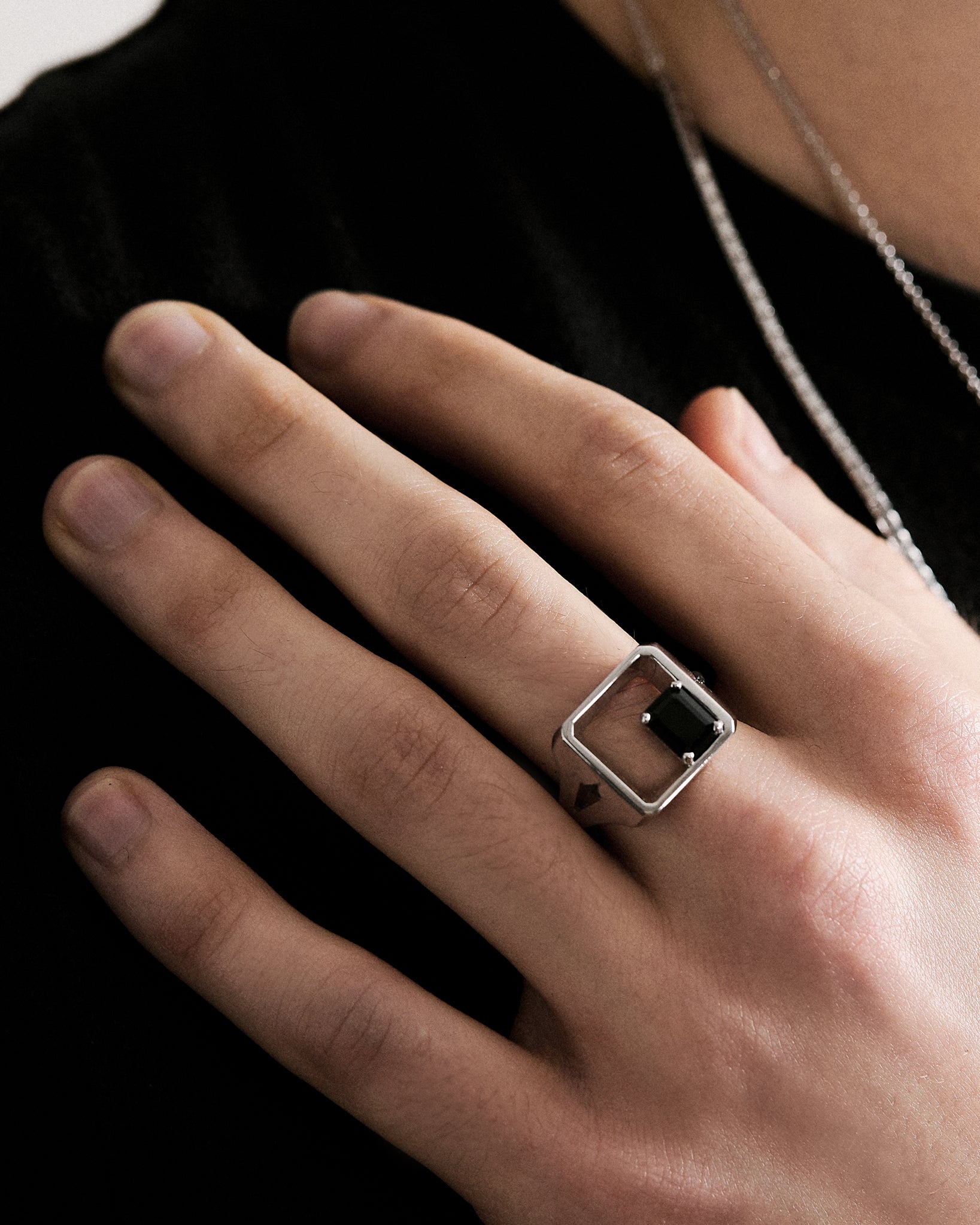 Hand wearing a silver signet ring with a black spinel gemstone on a dark background