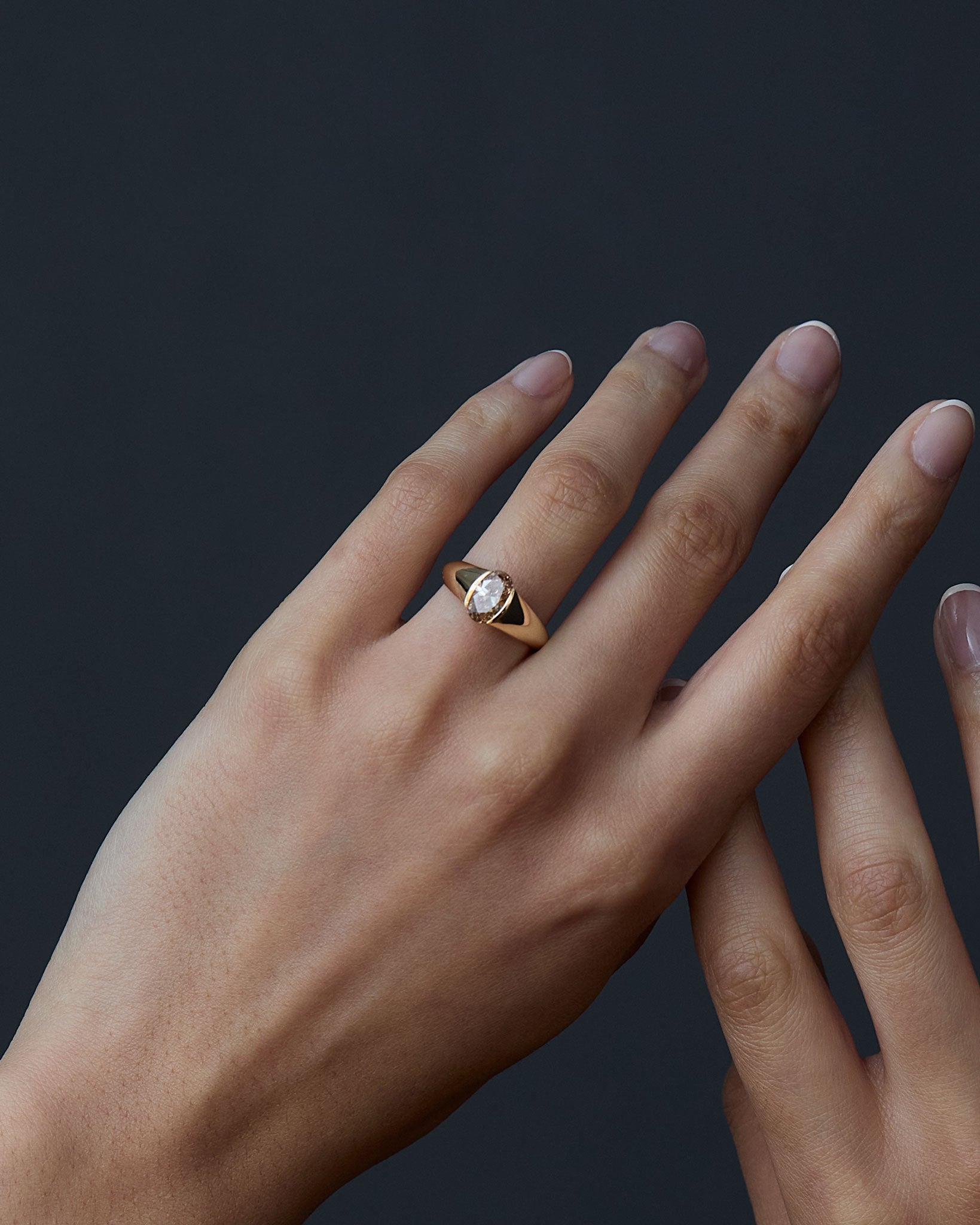 Hand wearing a gold ring with a Champagne diamond on a dark background