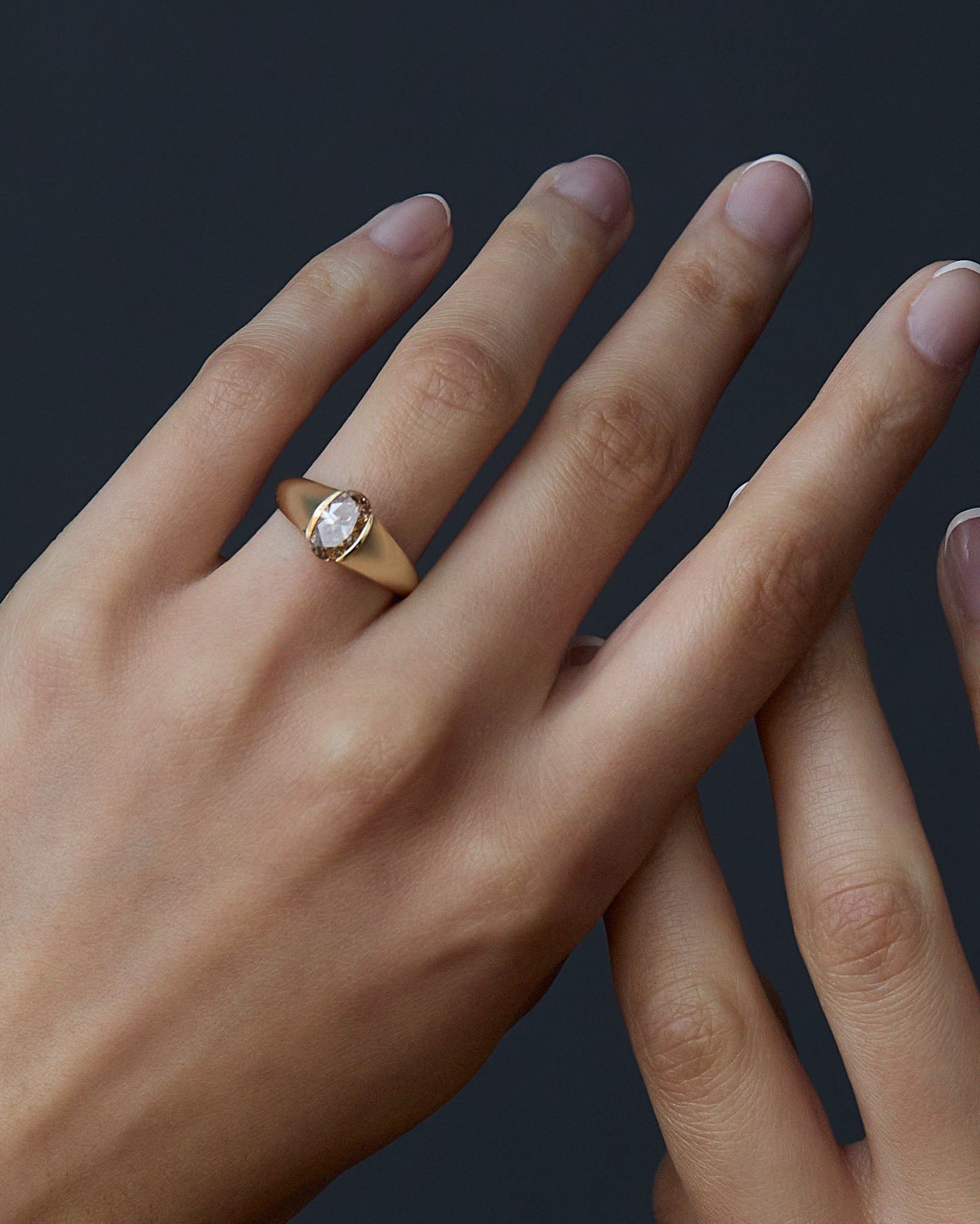 Gold ring with a diamond on a hand against a dark background