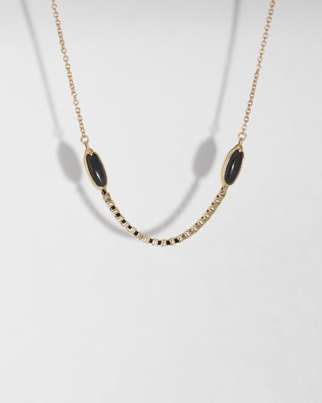 Gold necklace with black jade crescent shaped stones on a light gray background