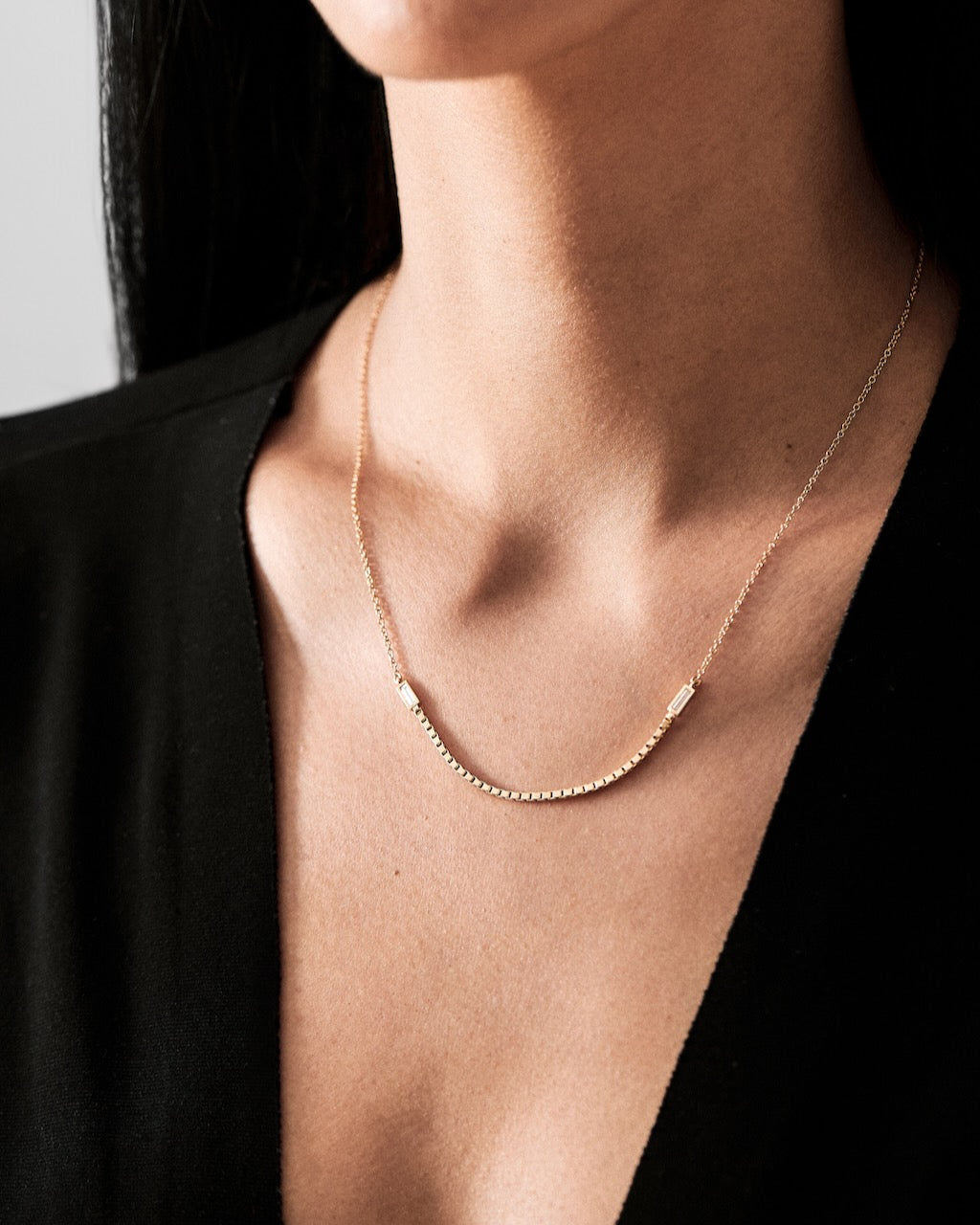 Gold necklace on a person wearing a black top against a neutral background