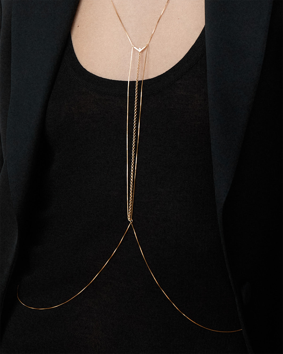 A close-up of a model wearing a Bliss Lau Interlude gold body chain over a black top.