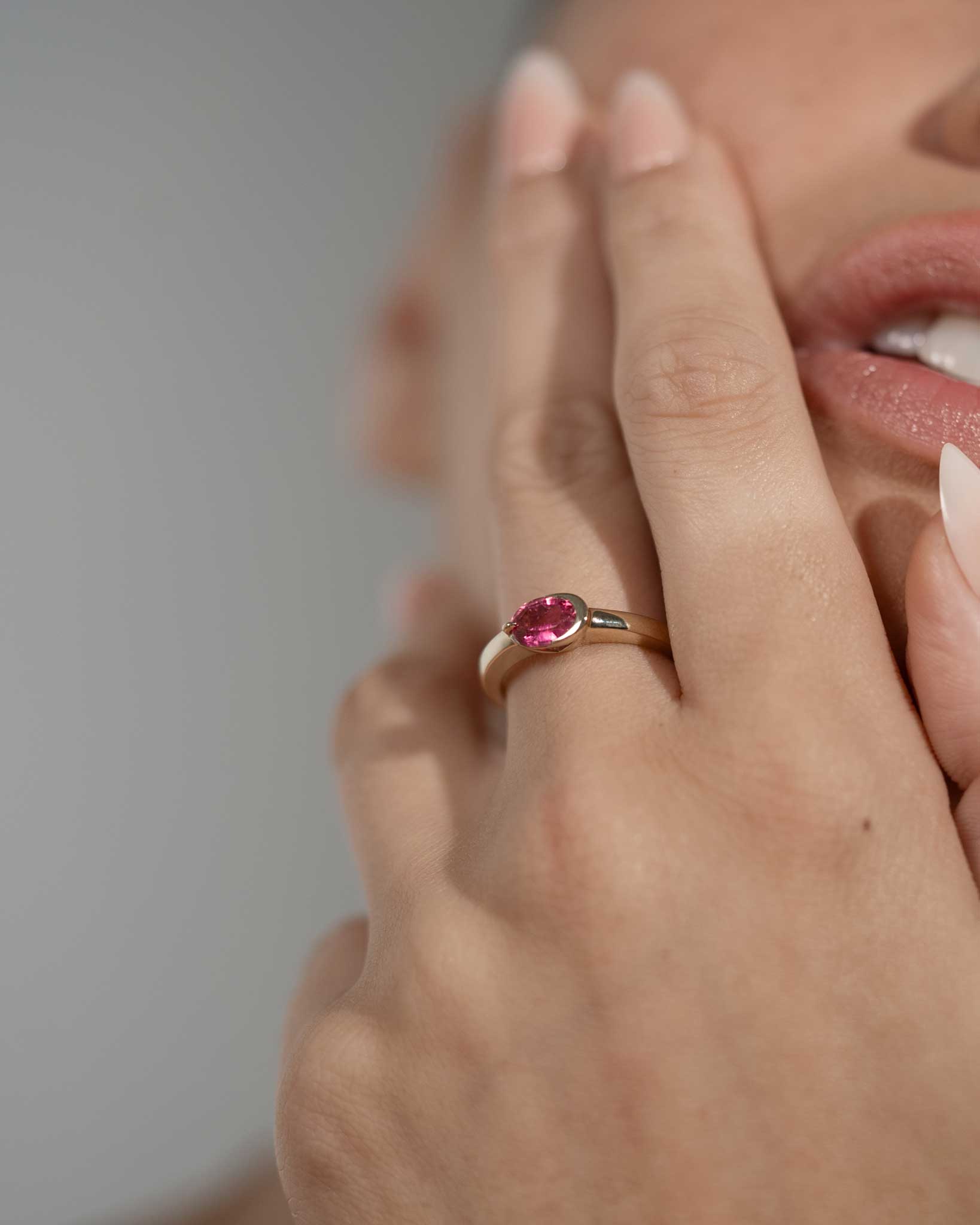 Close-up of a hand wearing a ring with a pink gemstone against a neutral background