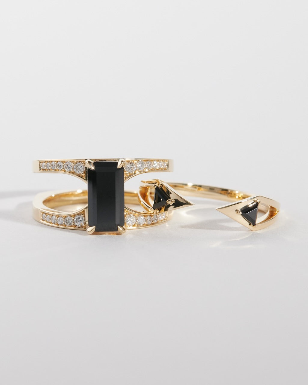 Set of 18k yellow gold interlocking rings with black spinel and pave diamonds on a light gray background