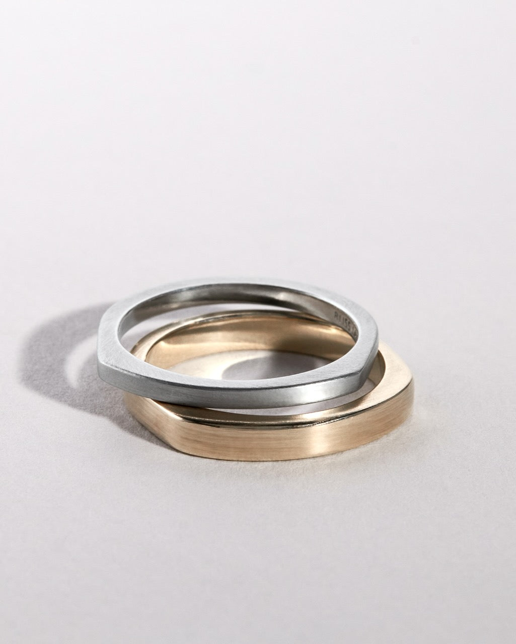 Two wedding band rings, one platinum and one gold, on a light gray background