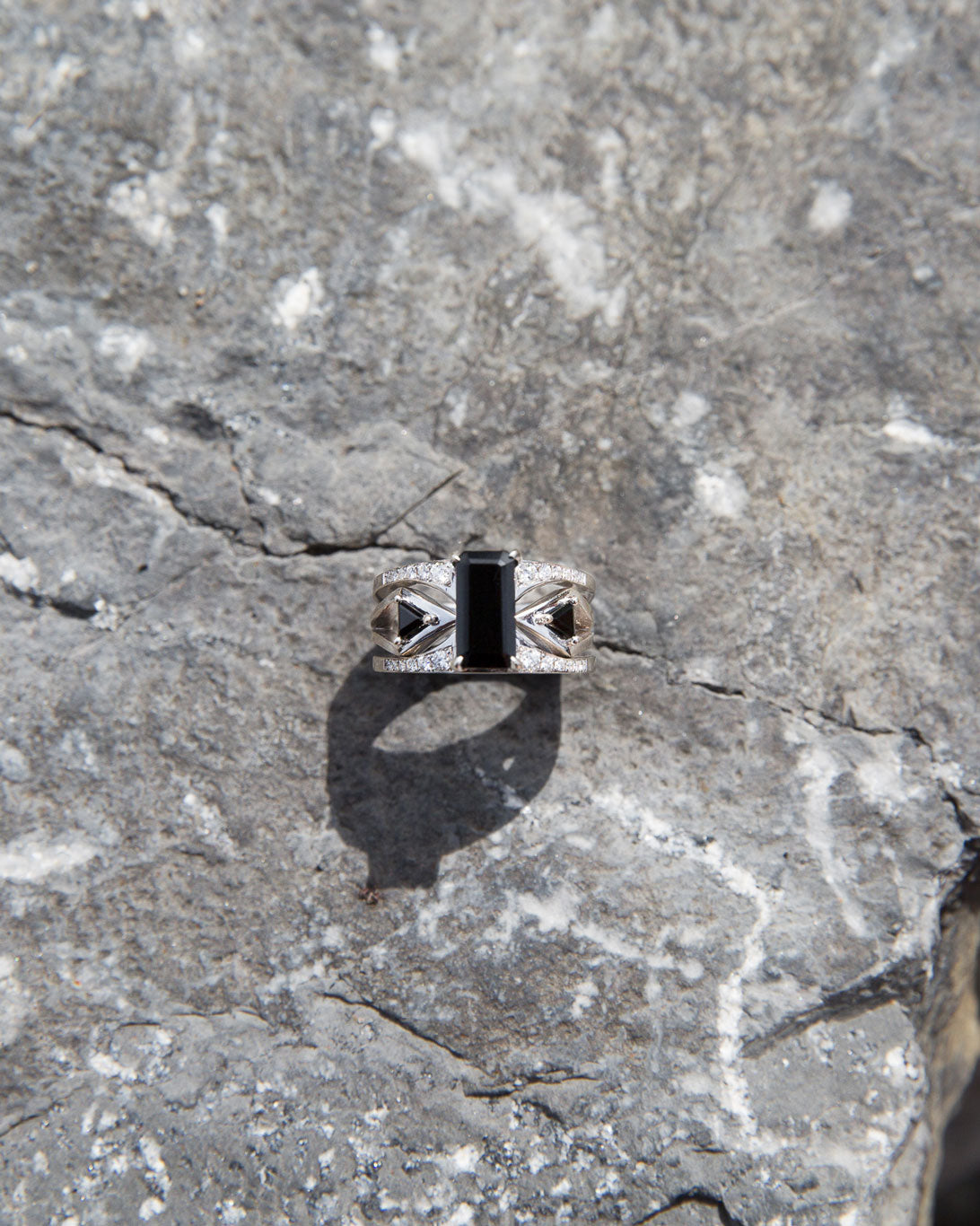 Artistic shot of the Mirage + Reflection Ring Set placed on a textured rock surface, emphasizing its luxury craftsmanship and stunning black spinel.