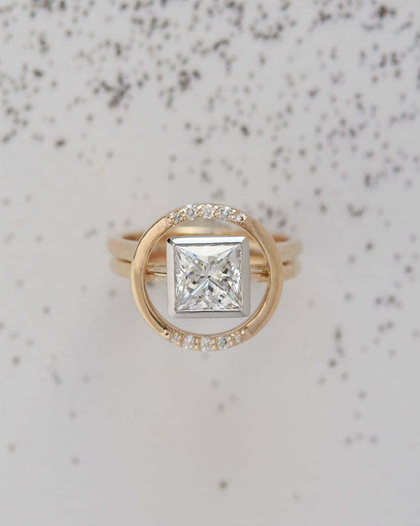 Luxury Royale Ring Set showcasing a dazzling princess cut diamond encircled by shimmering diamonds, elegantly positioned on a textured backdrop.