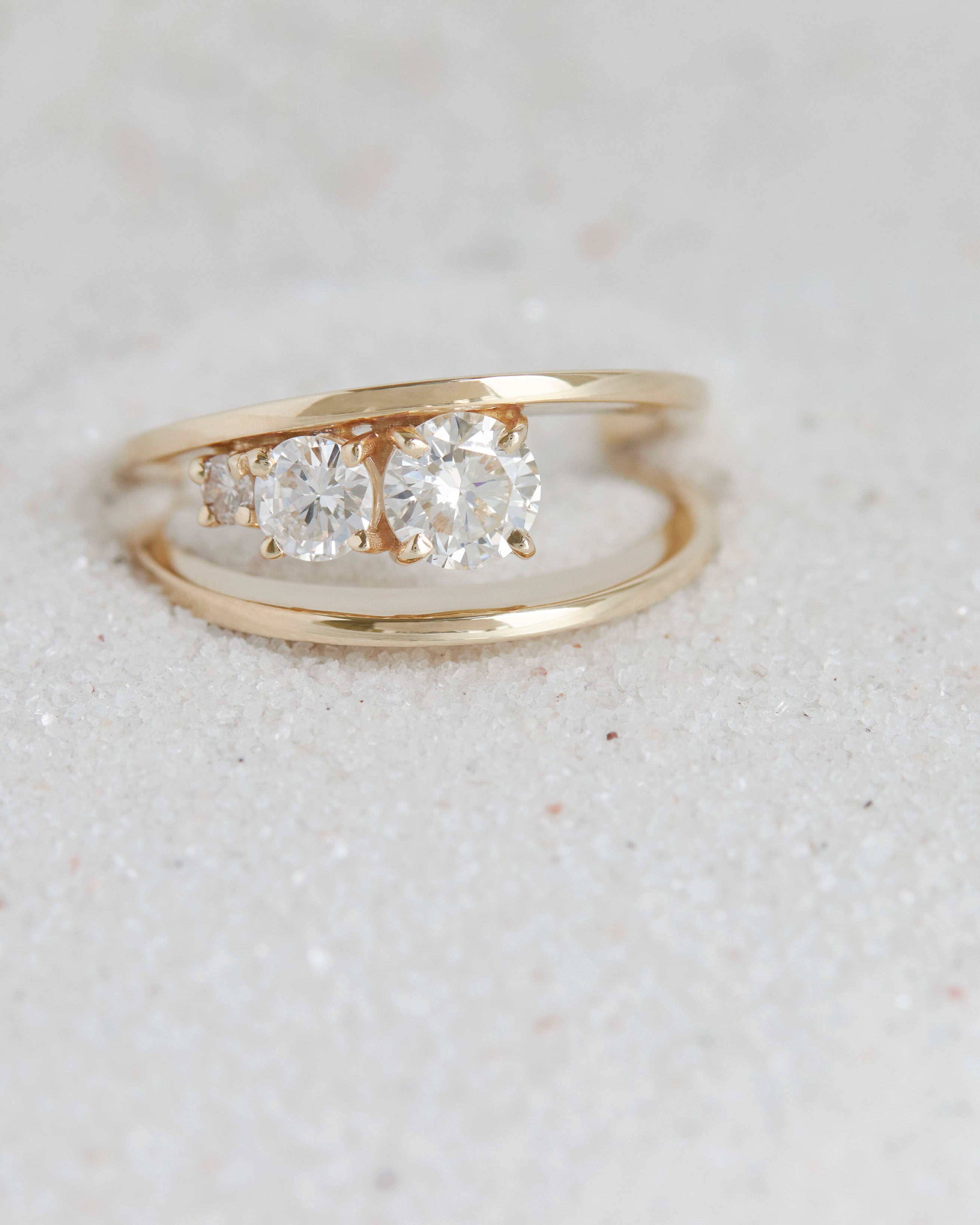 Close-up of the Empath Ring on soft sand, highlighting its exquisite diamonds and refined gold band.