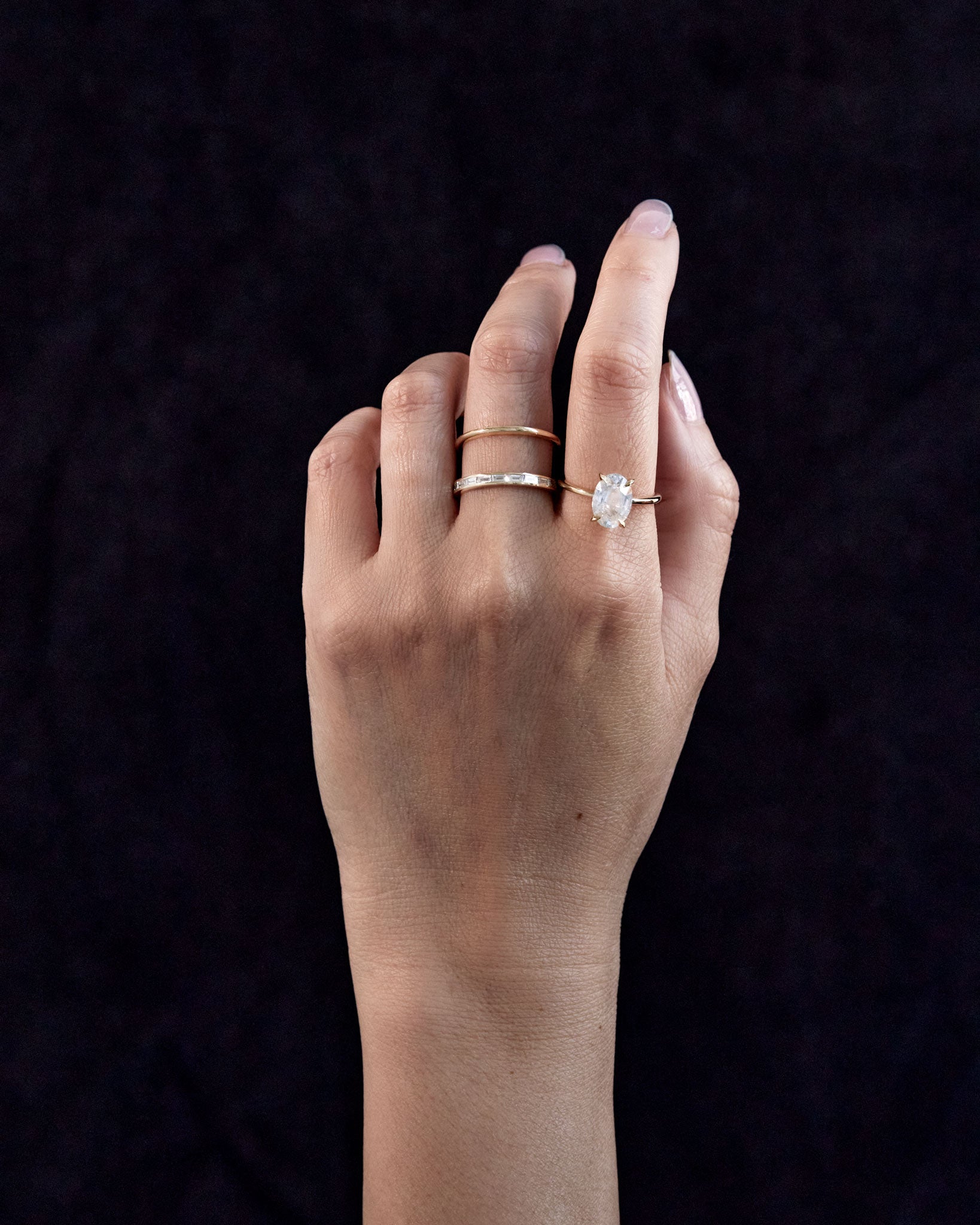 Cascade Enclose Ring displayed elegantly on a model's hand, featuring asymmetrical double gold bands with a diamond baguette in a luxurious setting.
