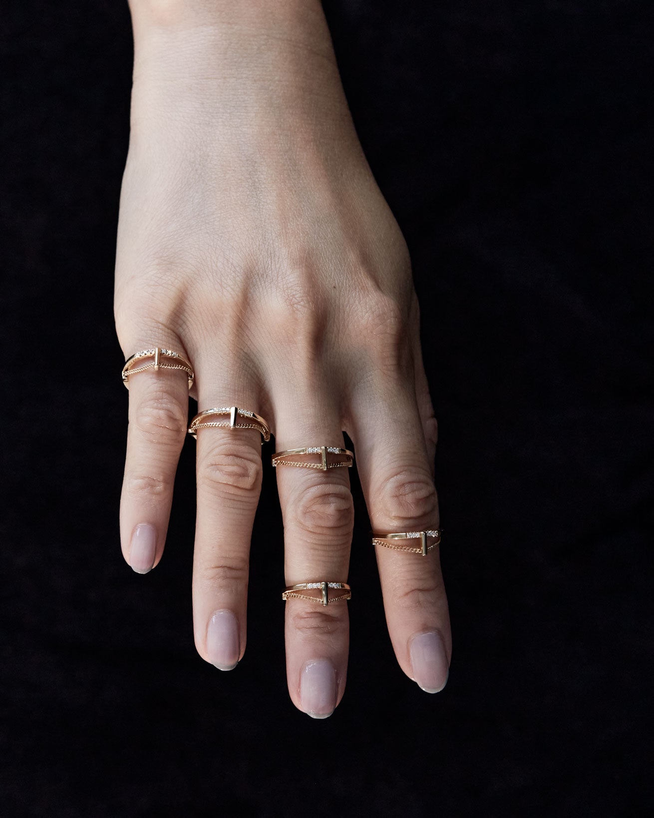 A hand adorned with several Pave Cusp Rings 18K, highlighting the unique geometric designs and luxurious finish in a stylish arrangement.