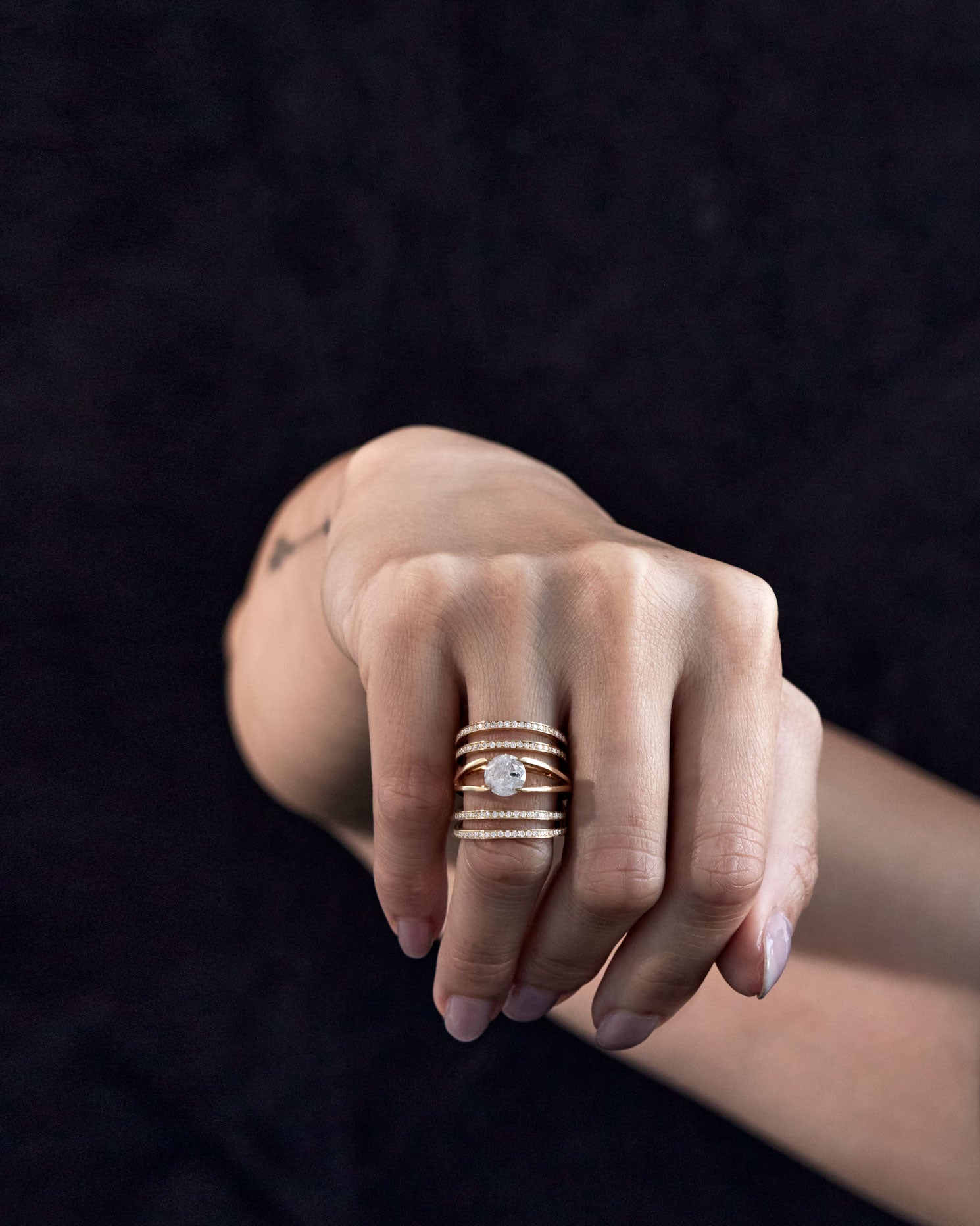 Elegant hand showcasing the Elliptical Enclose Ring Set + Centered Ring by Bliss Lau, accentuated with shimmering diamonds along multiple bands against a dark background.