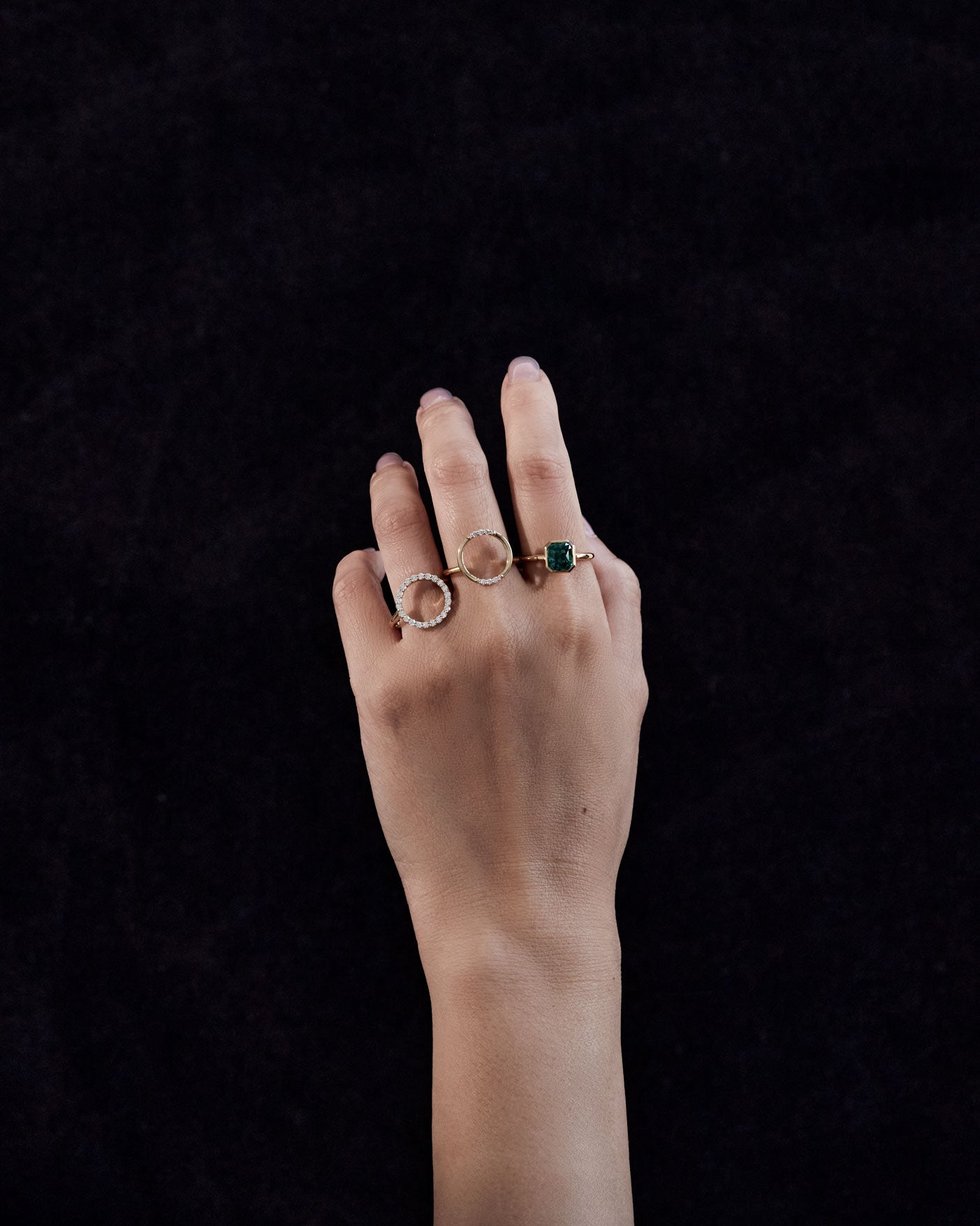 The Royale Ring Set displayed on a hand, showcasing two exquisite rings, one with a green gemstone and the other a delicate pave diamond design, against a dark backdrop.