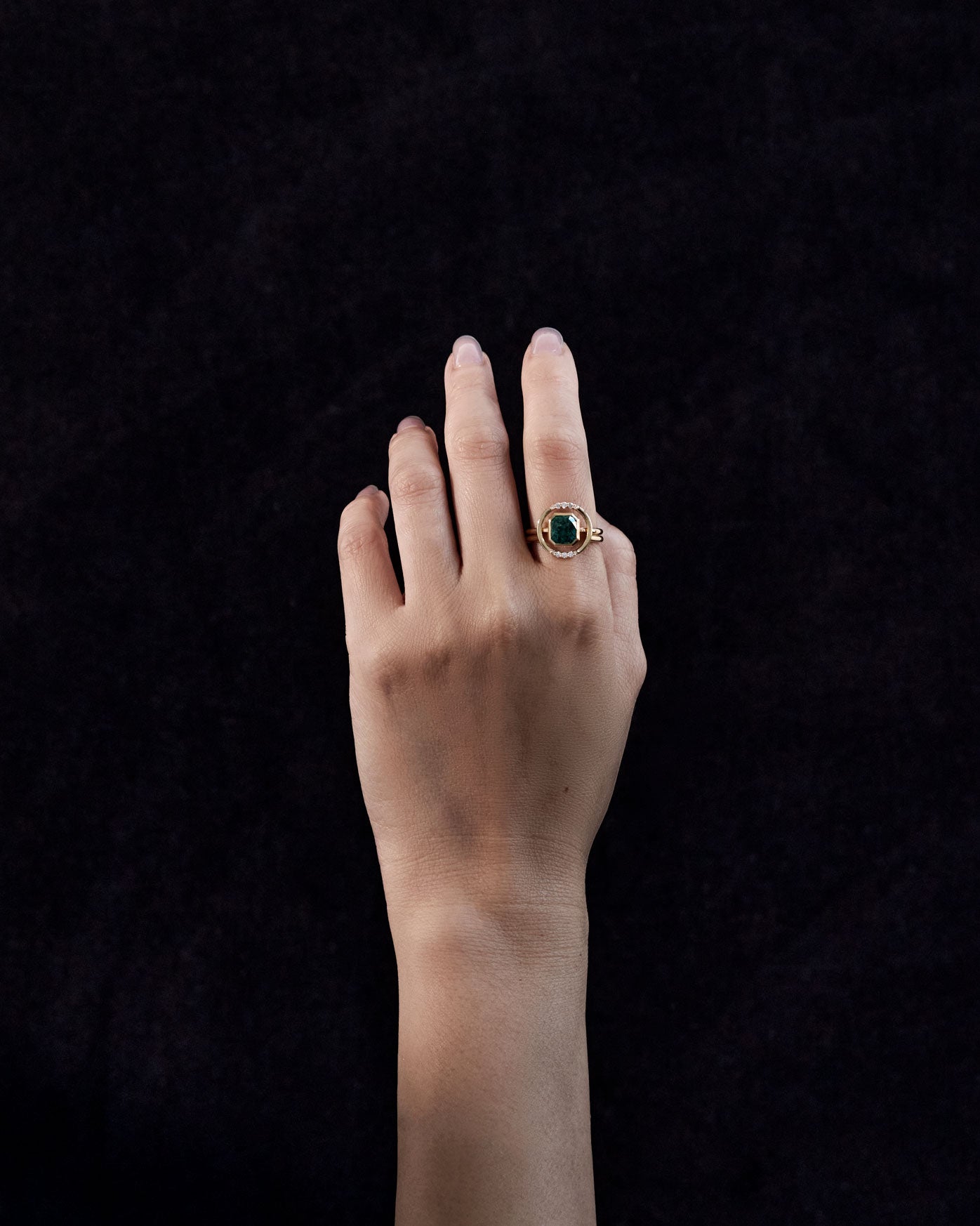 Elegant Royale Ring Set showcased on a hand with a dark background, featuring a stunning green gemstone surrounded by a delicate halo of diamonds.