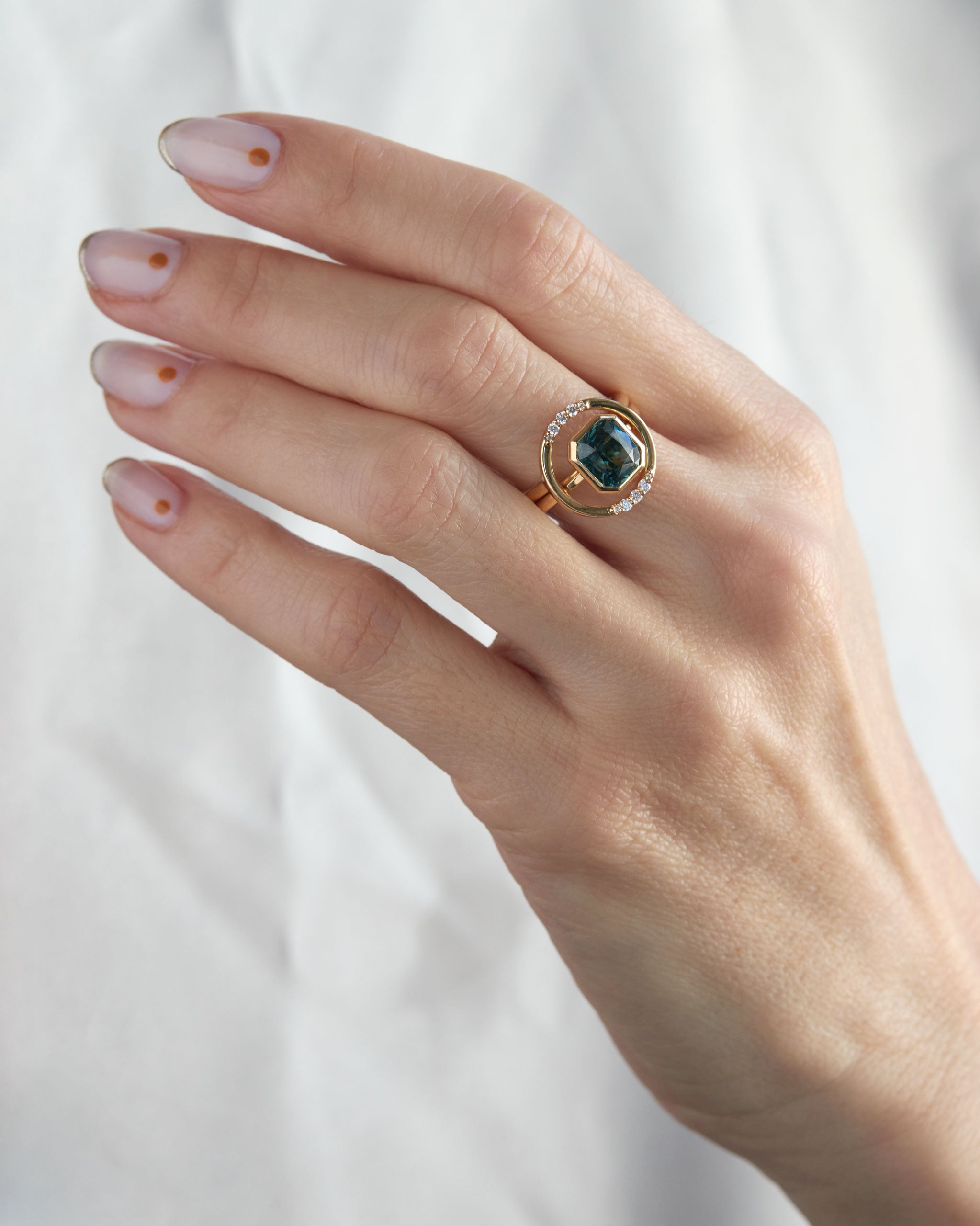 Close-up of the Royale Ring Set on a hand, highlighting the luxurious green gemstone ring surrounded by a halo of sparkling diamonds, set against a soft white background.