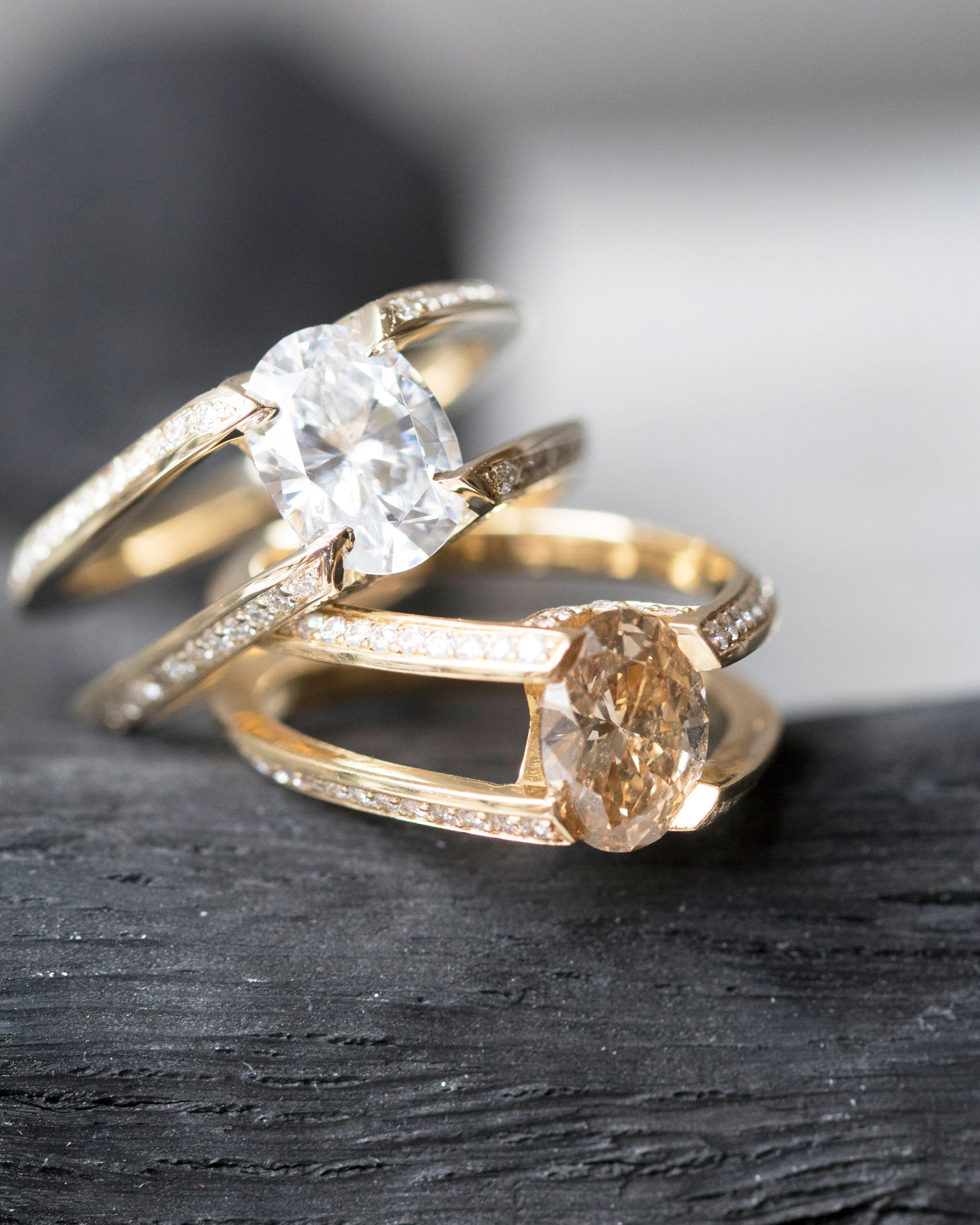 Two Futurist Engagement Rings from the Signature Collection, elegantly displayed with one showcasing a white diamond and the other a warm champagne diamond, both in stunning yellow gold.