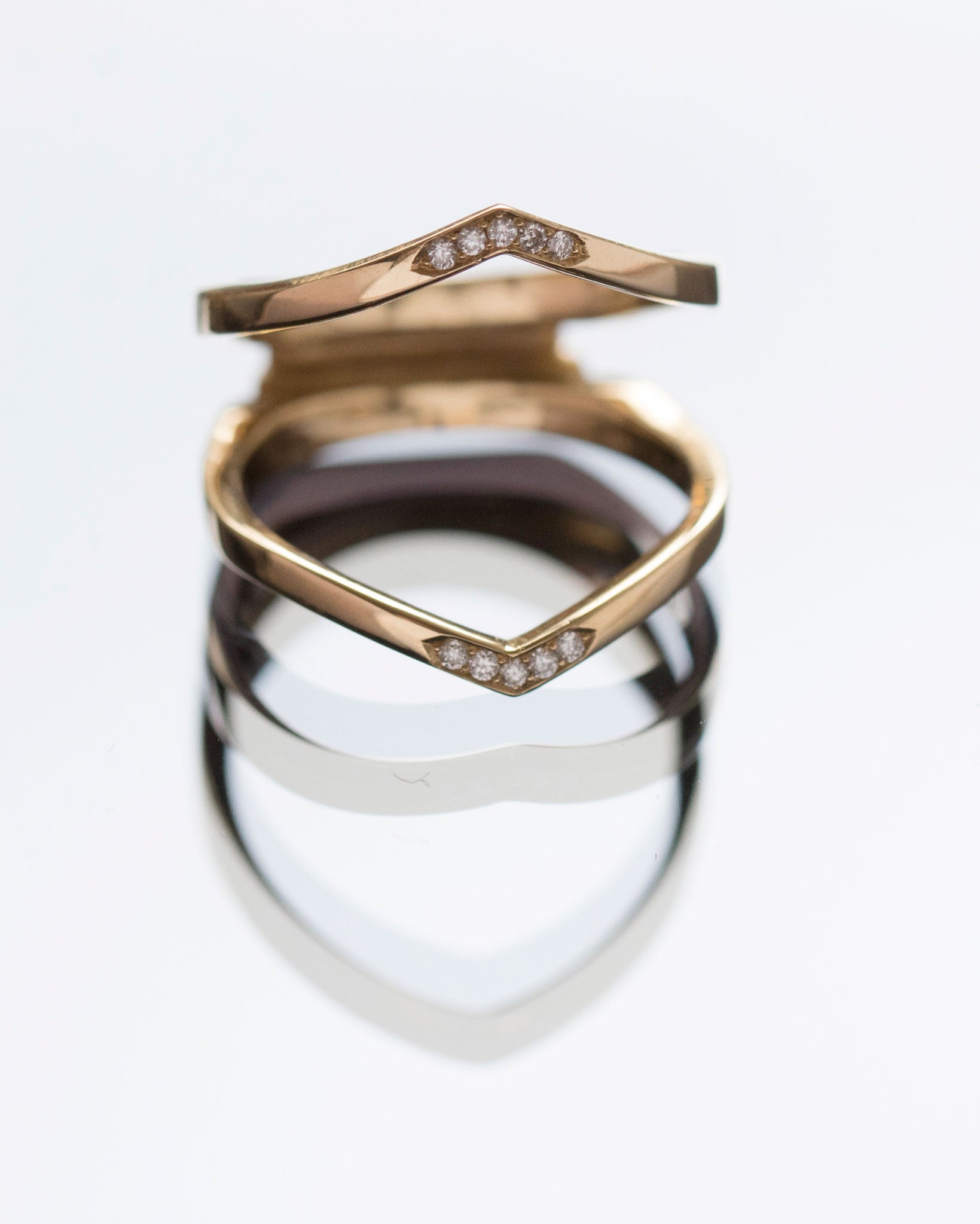 Two exquisite Oblique X Enclose Bands displayed with a reflection, featuring pave set diamonds and a chic gold finish.