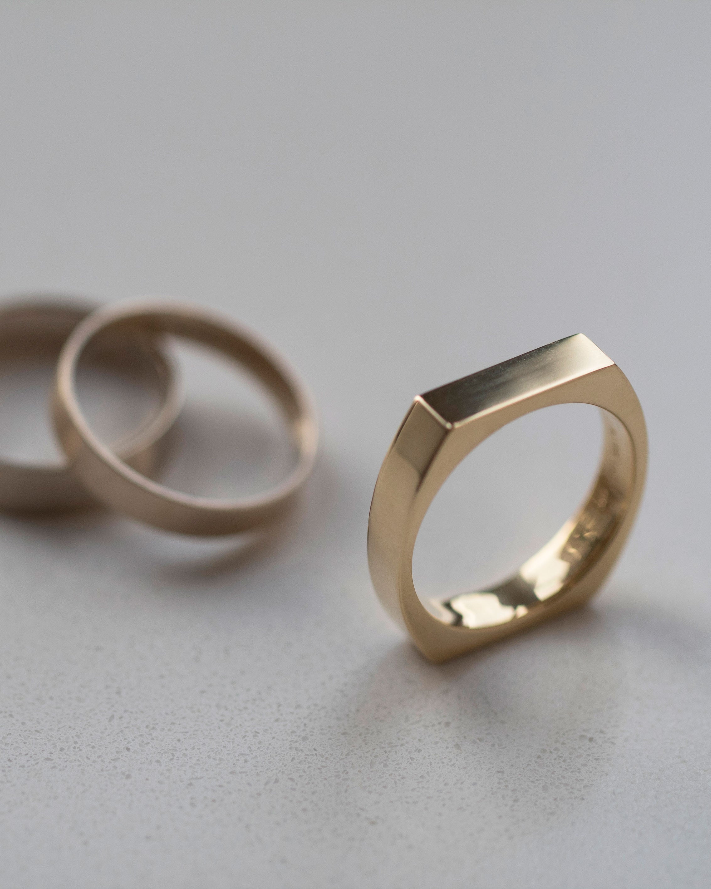 Rational V Band by Bliss Lau, a luxurious gold ring showcased elegantly with two additional rings, highlighting its unique design and finish.