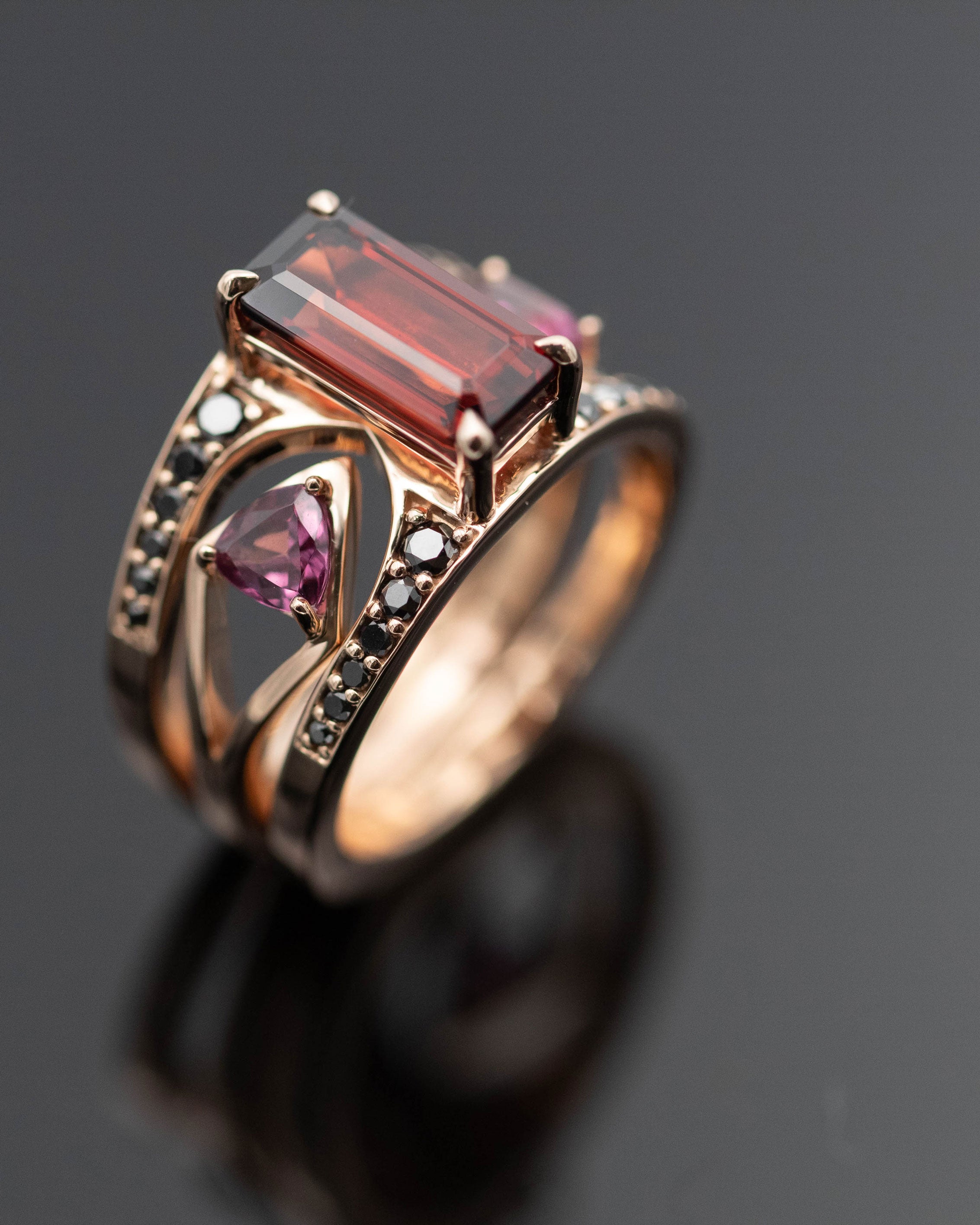 Close-up view of the Mirage + Reflection Ring Set Garnet highlighting its stunning rose gold setting and intricate details, featuring a central dark garnet and supporting gemstones.