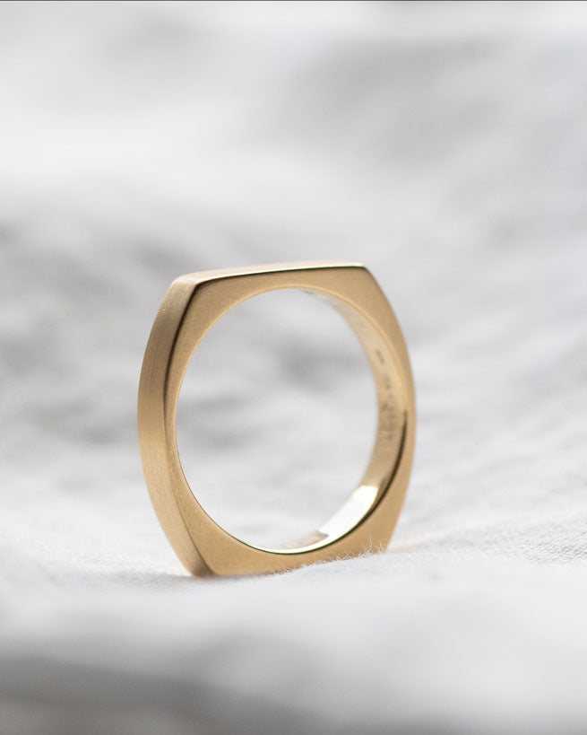 Close-up of the Rational V Band by Bliss Lau, featuring a stunning gold finish in a sophisticated square shape, set against soft fabric.