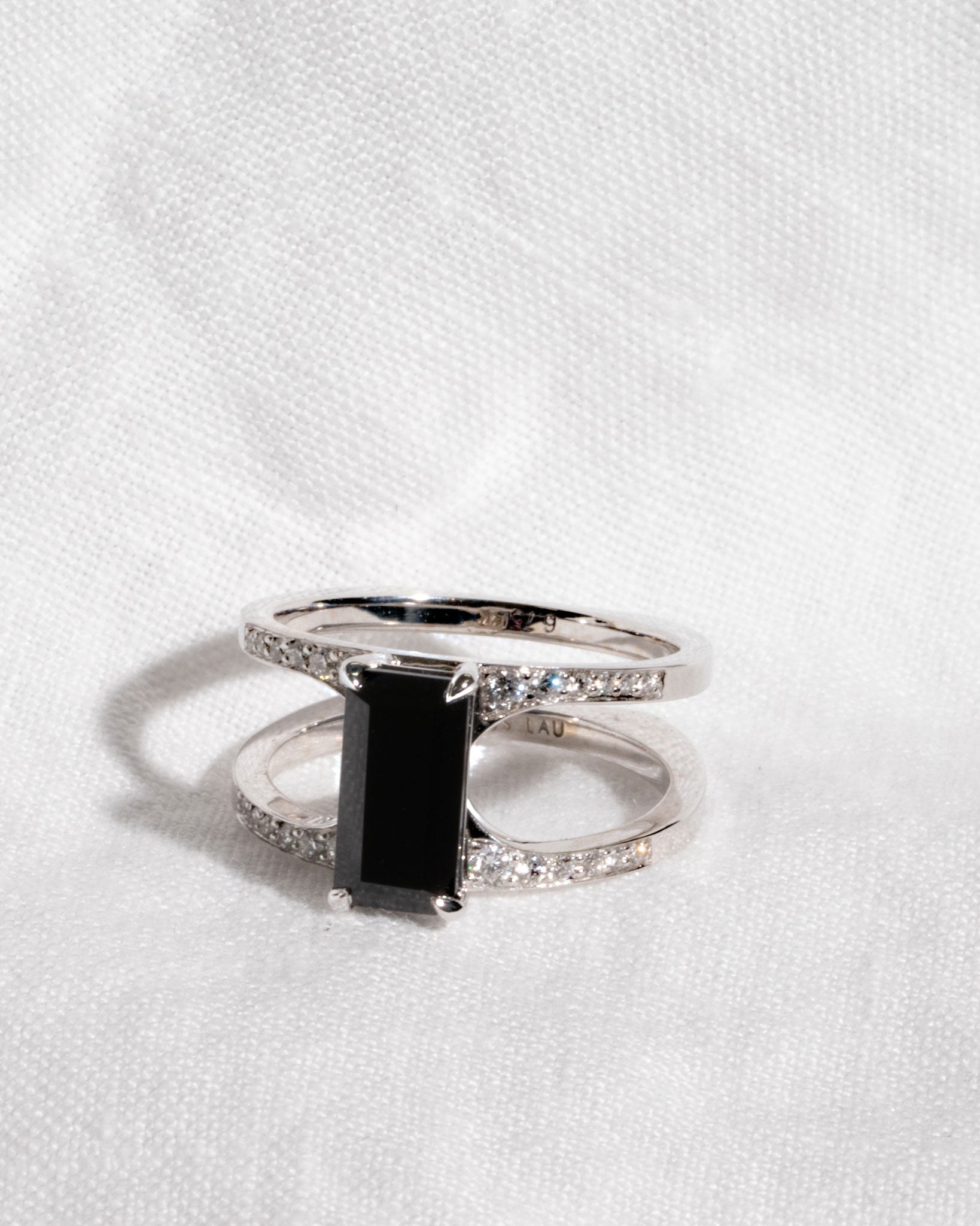 Intricate Mirage Ring in white gold featuring a striking emerald-cut black diamond, elegantly displayed on soft fabric.
