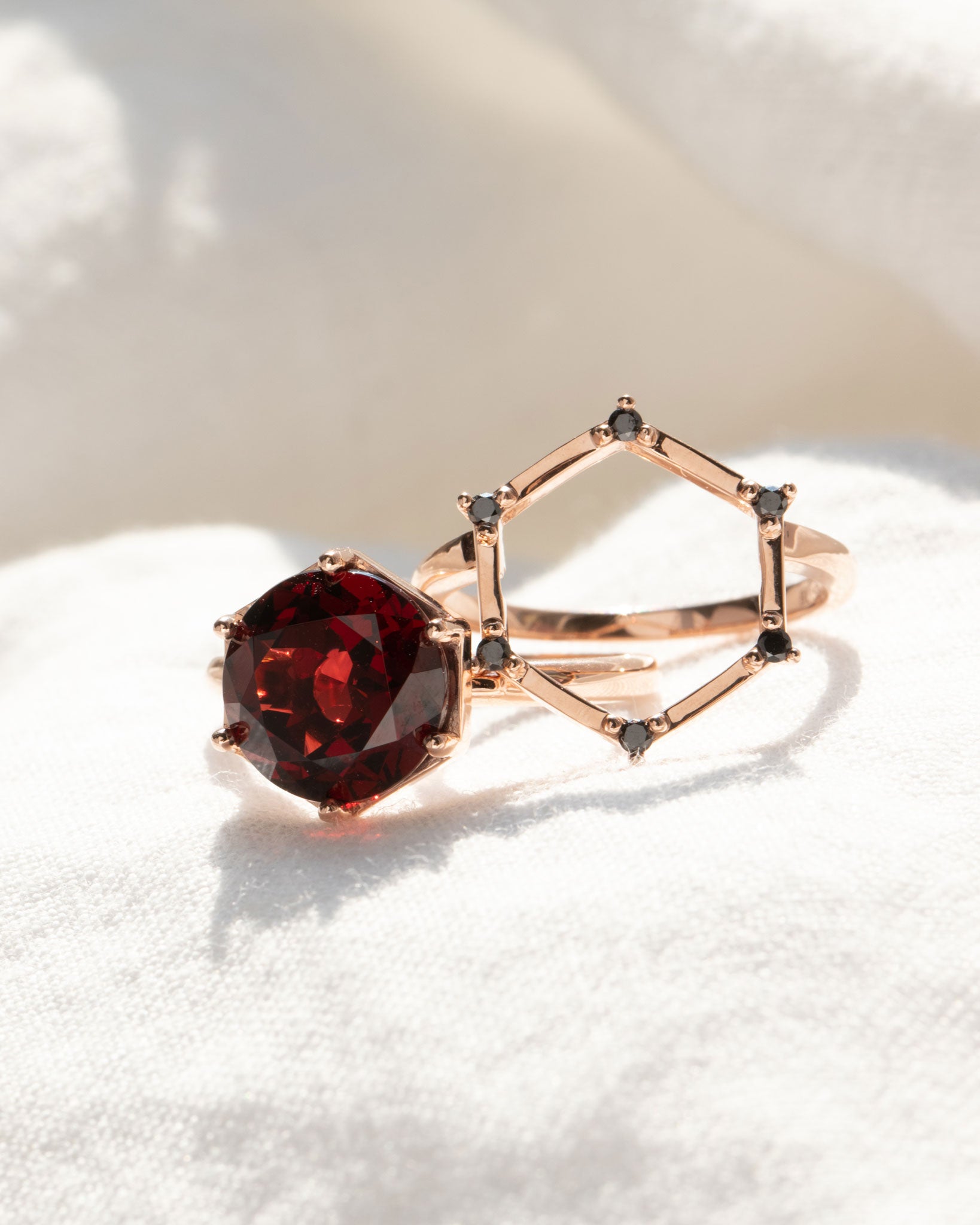 Aura Ring Wedding Ring Set artistically arranged on soft fabric, emphasizing the beautiful interplay of red garnet and black diamonds in a luxurious design.
