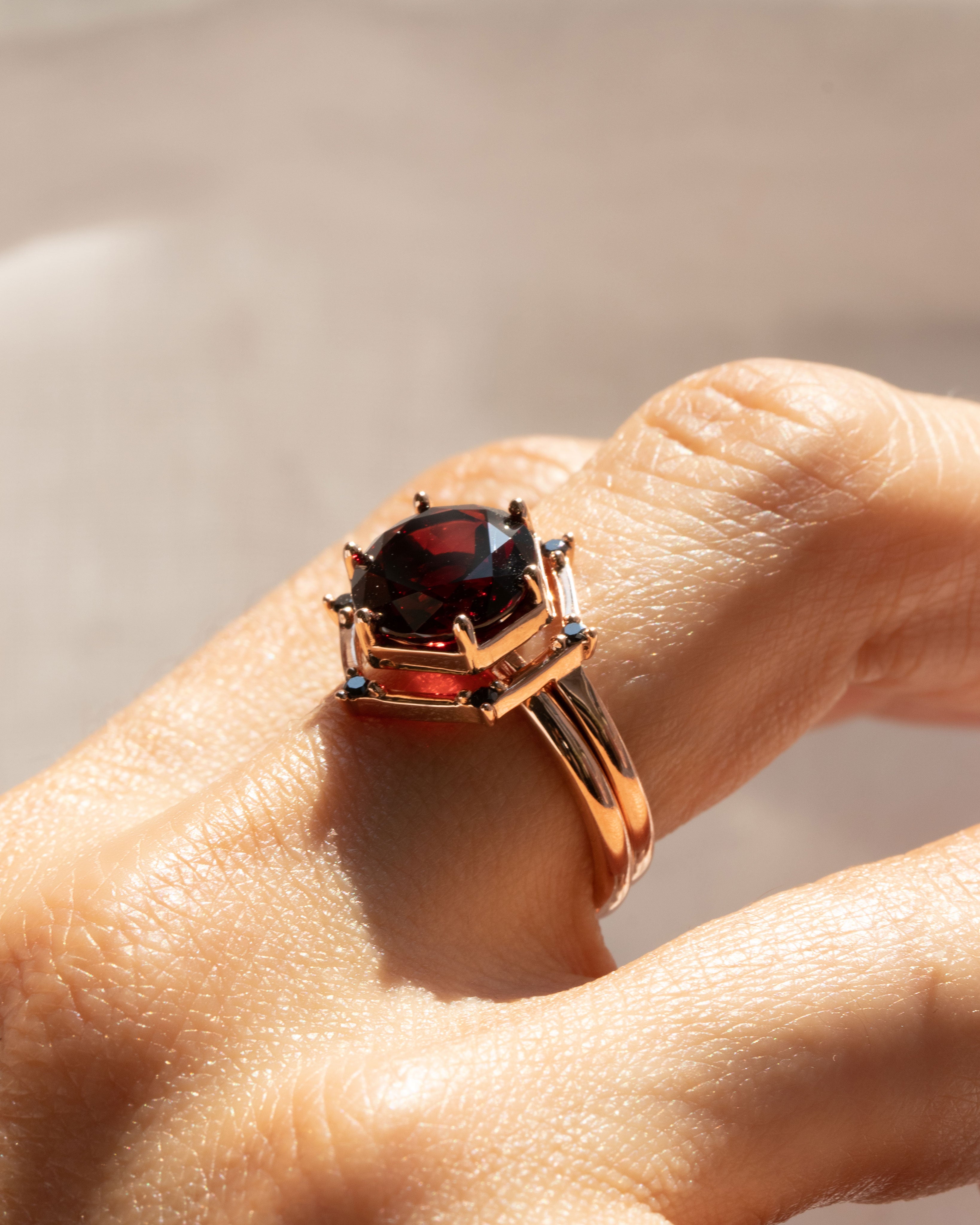 Close-up view of the Aura Ring Wedding Ring Set showcasing a captivating oval Red Garnet amidst conflict-free black diamonds, beautifully crafted in recycled gold for a luxurious touch.