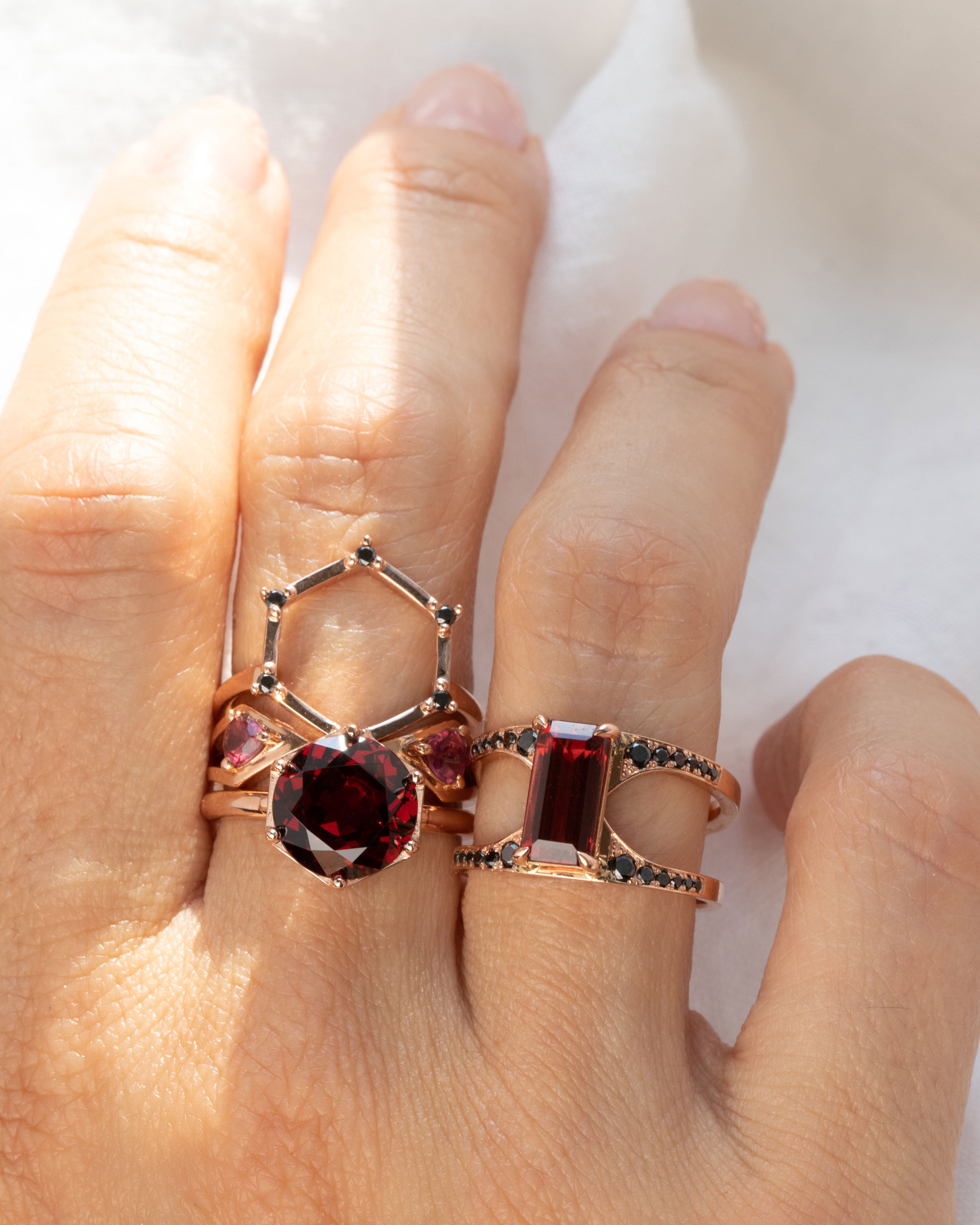 Elegant Aura Ring Wedding Ring Set displayed on a hand, highlighting the unique interlocking design and the stunning red garnet surrounded by conflict-free black diamonds.