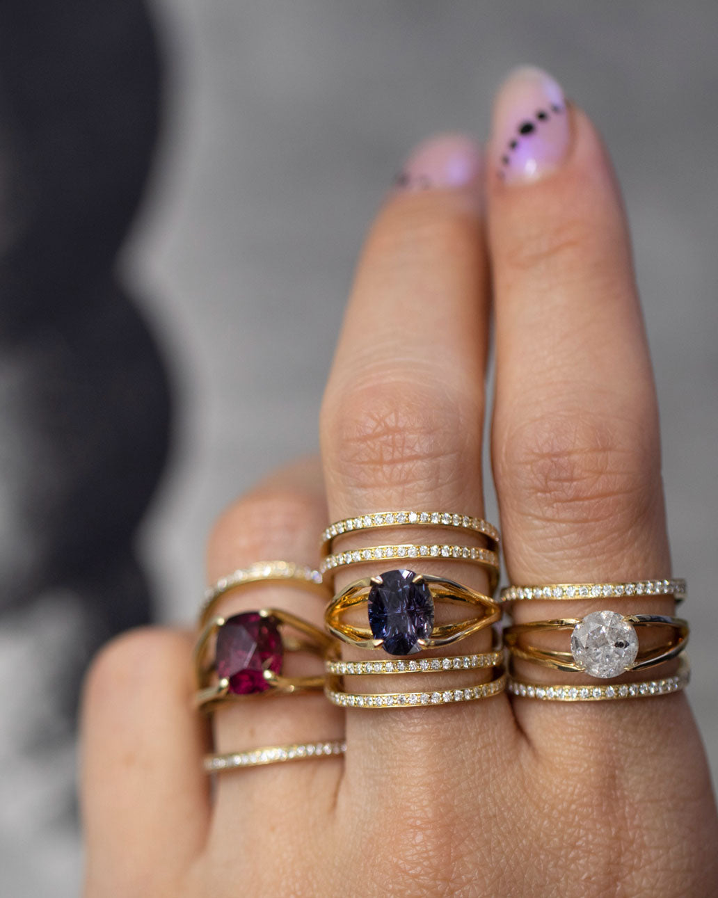 Chic display of the Elliptical Enclose Ring Set + Centered Ring by Bliss Lau, worn on fingers showcasing vibrant gemstones including a ruby and sapphire, beautifully set in gold.