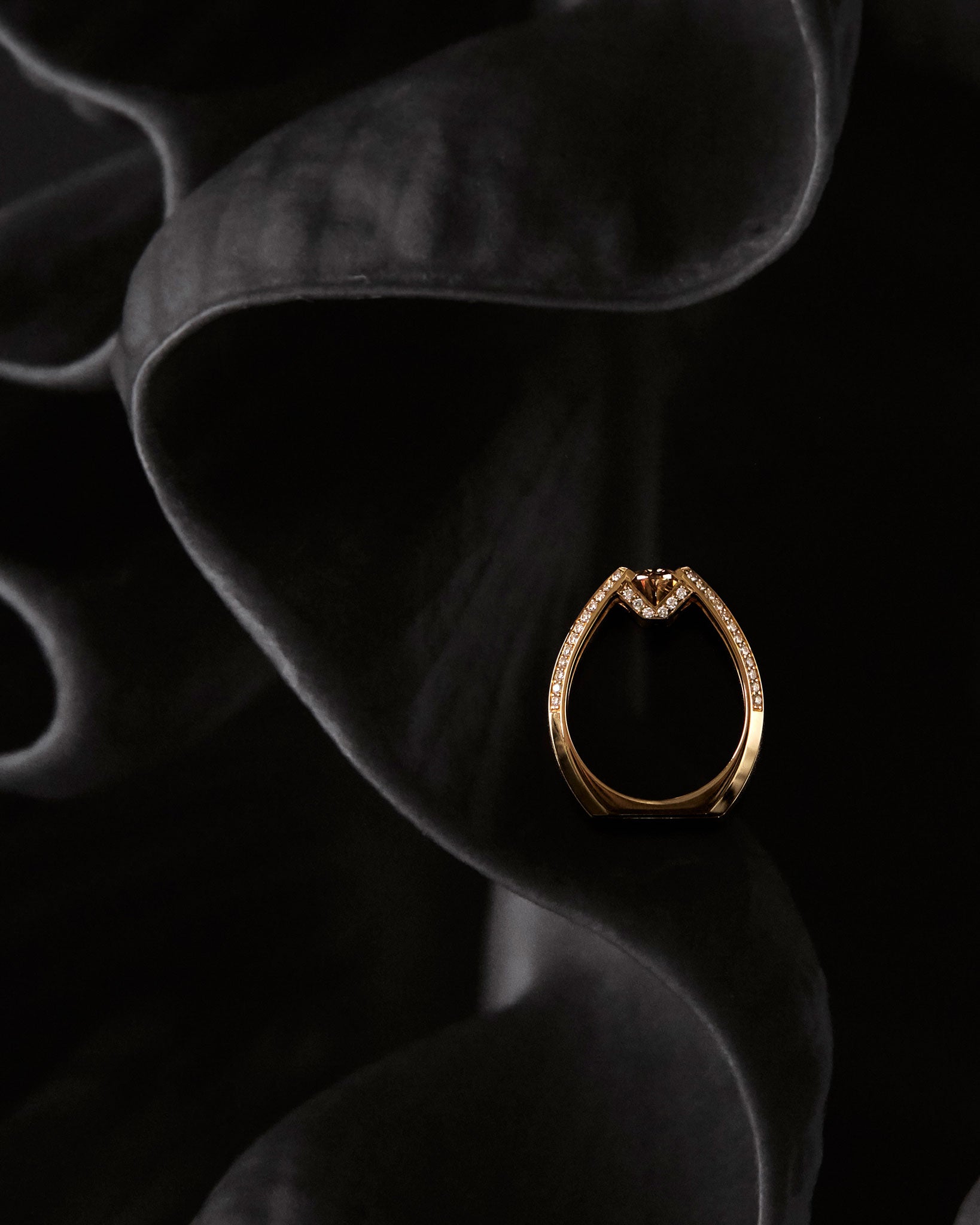 The Futurist Engagement Ring from the Signature Collection gracefully poised on dark fabric, showcasing its luxurious design in yellow gold with sparkling diamond embellishments.