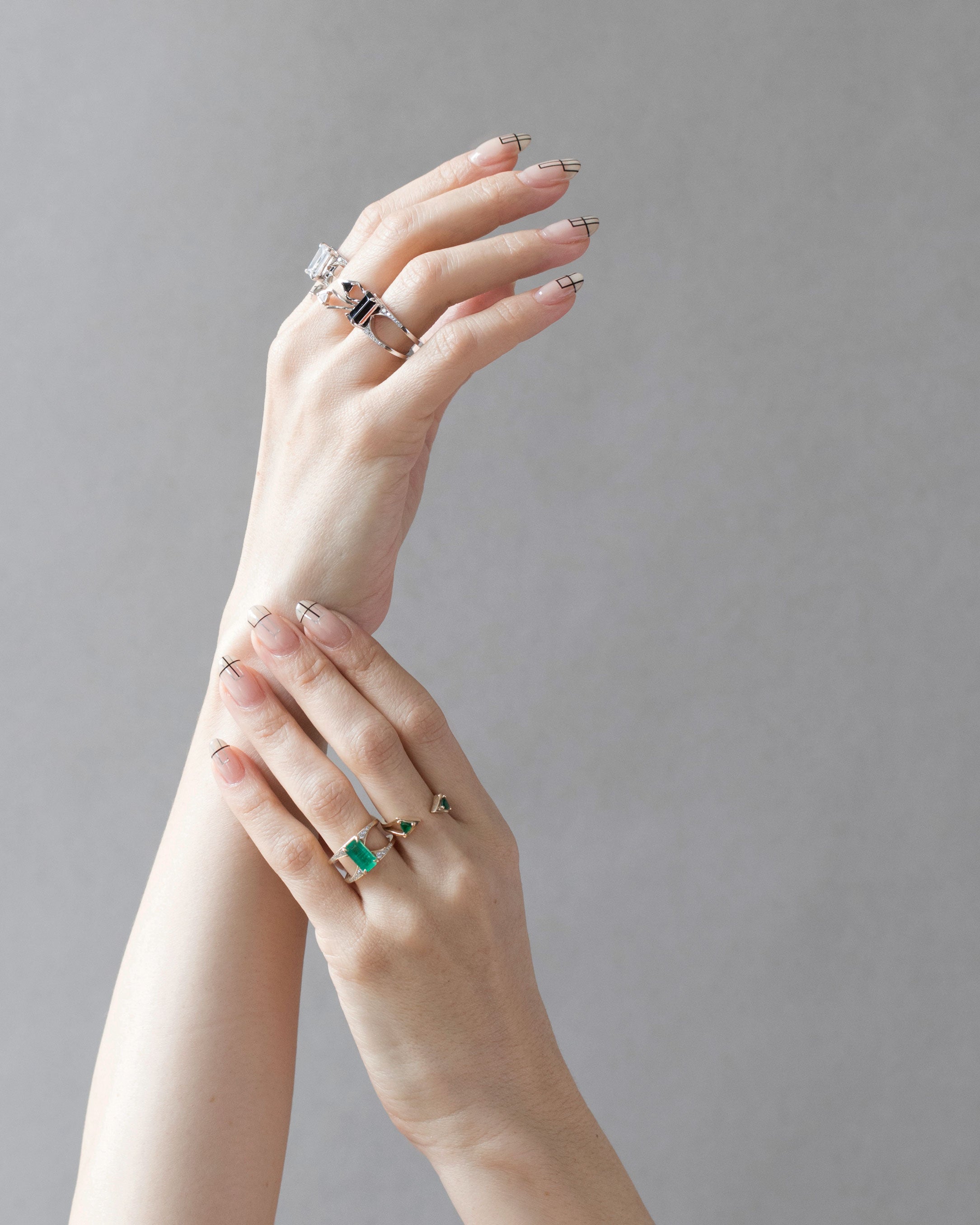 Elegant display of hands adorned with the Mirage + Reflection Ring Set Emerald, featuring intricate interlocking designs and stunning emerald gemstones.