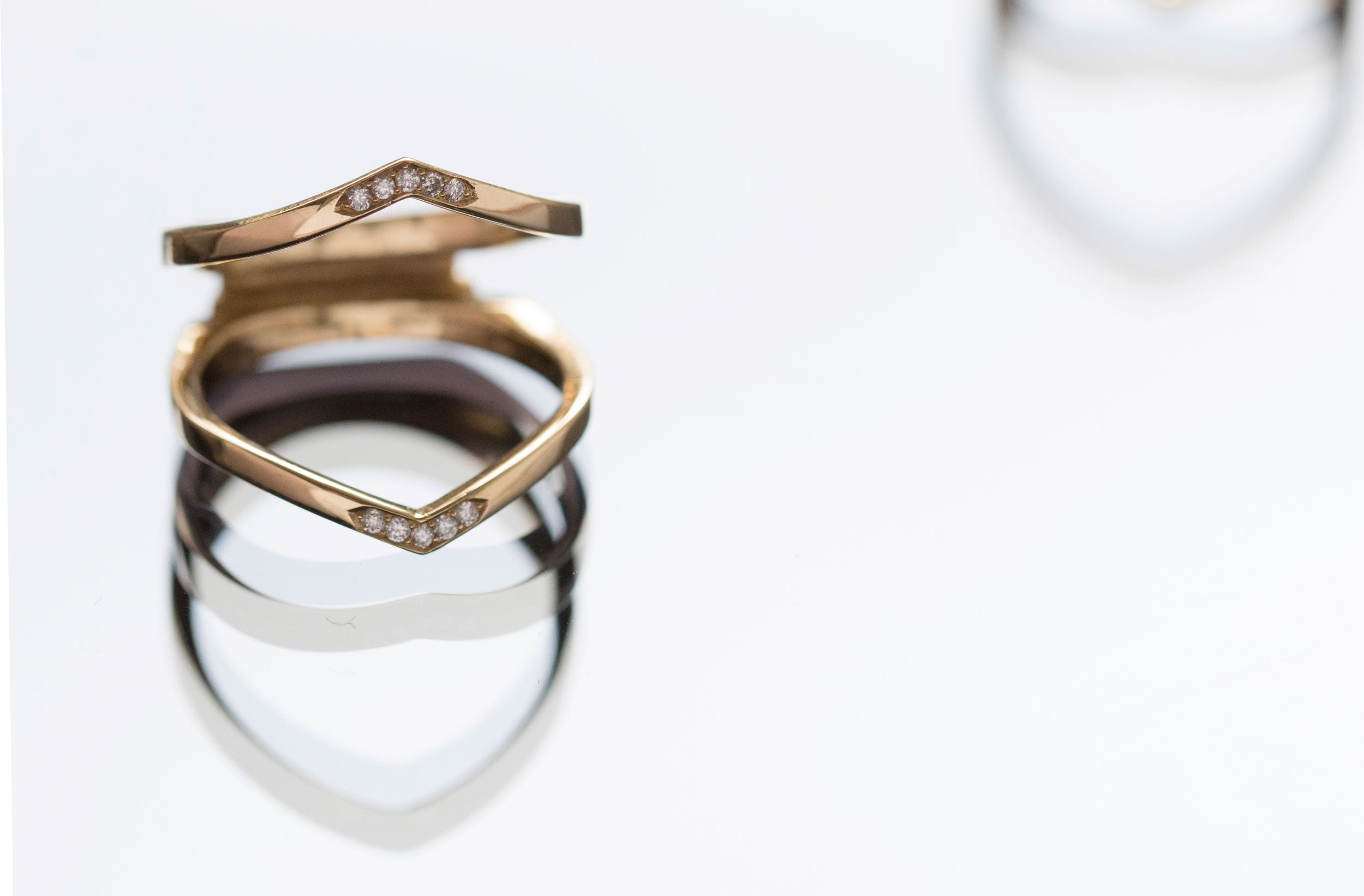 Elegant interlocking wedding bands displayed on green leaves, showcasing intricate designs with sparkling pavé accents in gold. Perfect for symbolizing timeless love and commitment.