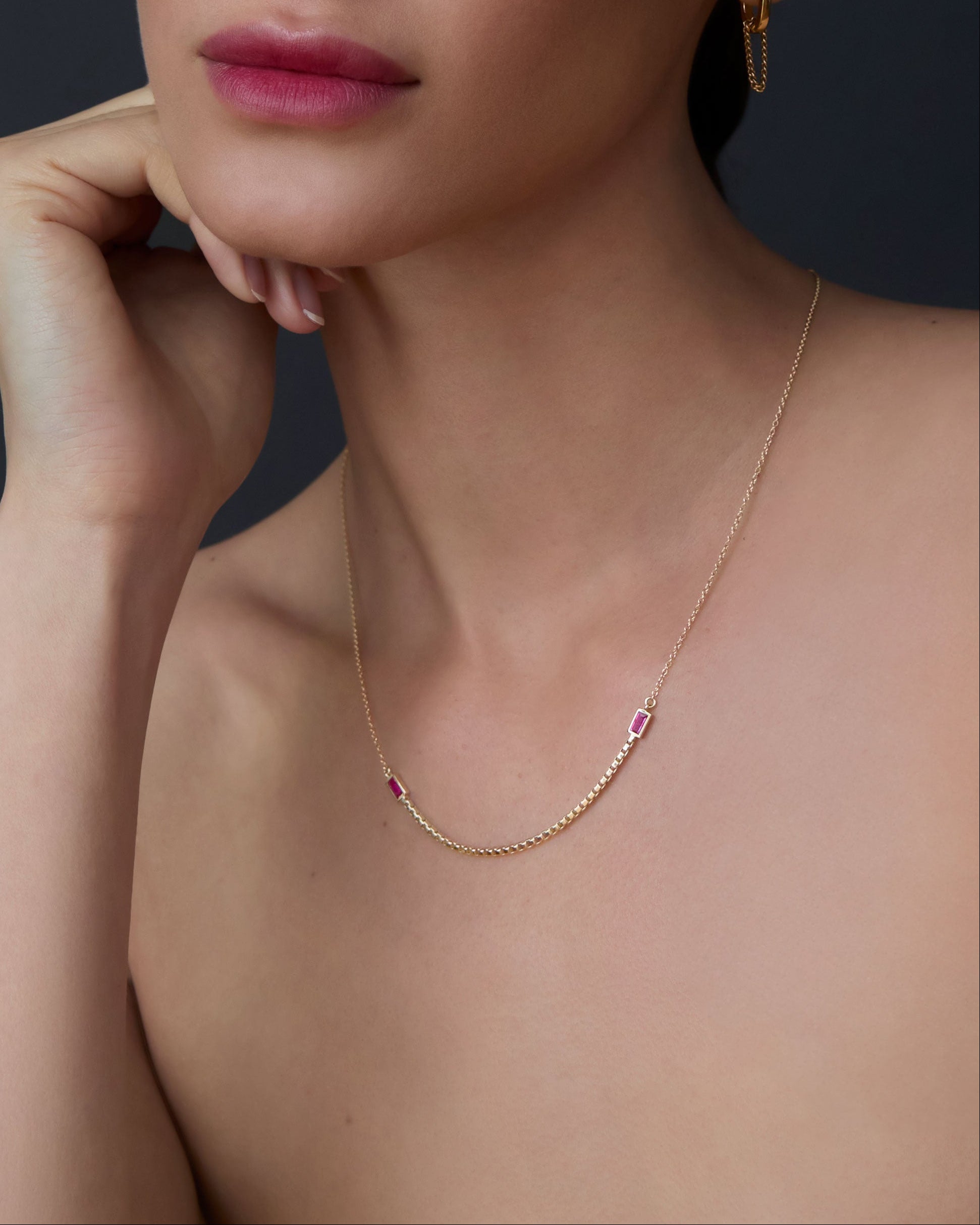 Close-up of a woman wearing a gold necklace with ruby gemstones against a dark background Halo