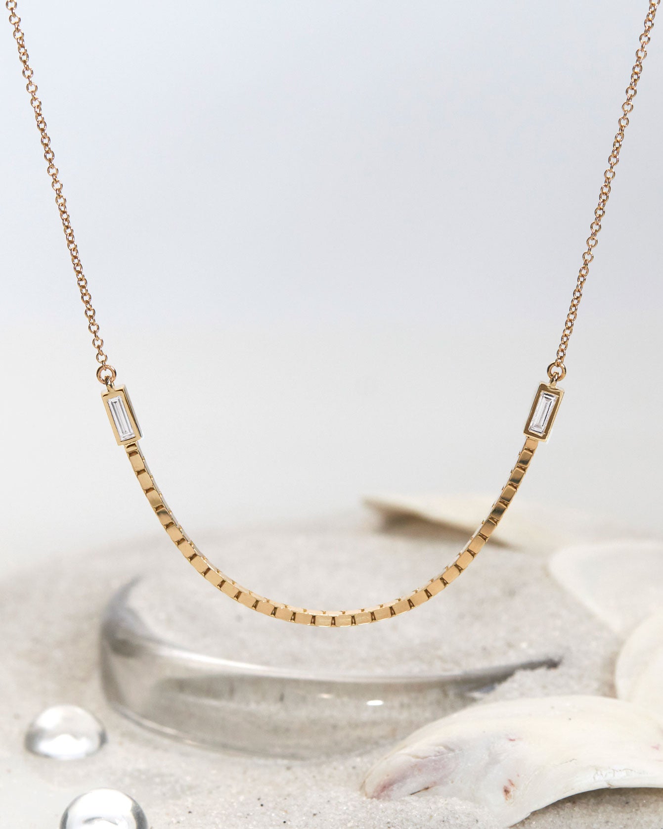 Bliss Lau Halo Luna Necklace close up with sand is a combination of interlick chain and box chain with the box chain hanging perfectly centered and two lab diamond baguettes on either side. 