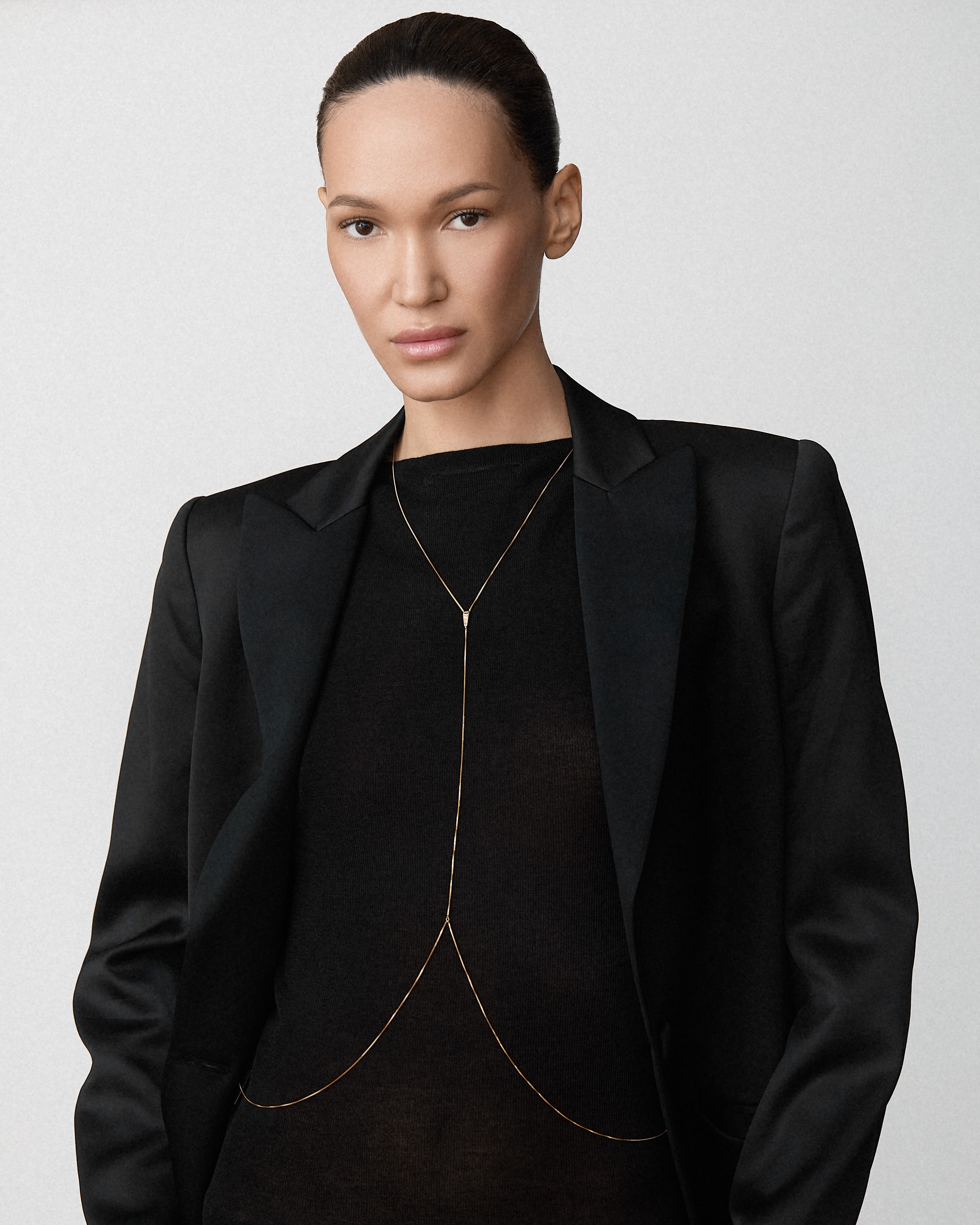 A model wearing a Bliss Lau gold body chain, a black satin blazer over a black top, 